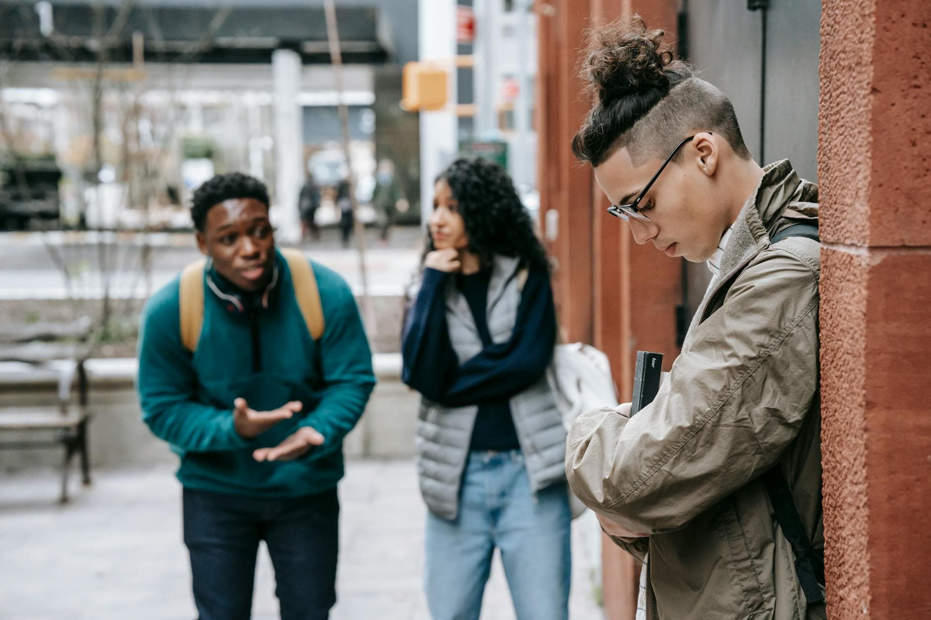 Side view of young student in glasses carrying book while standing in front of multiracial classmates - active listening in relationships