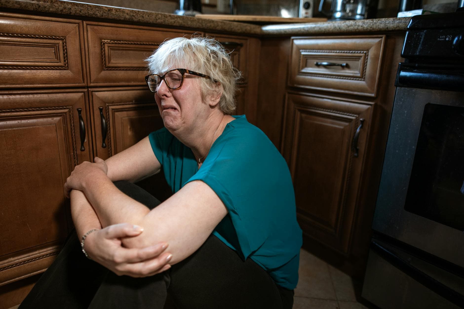 A distressed woman sitting on the kitchen floor, expressing deep emotion. - charlie sheen mental health struggles