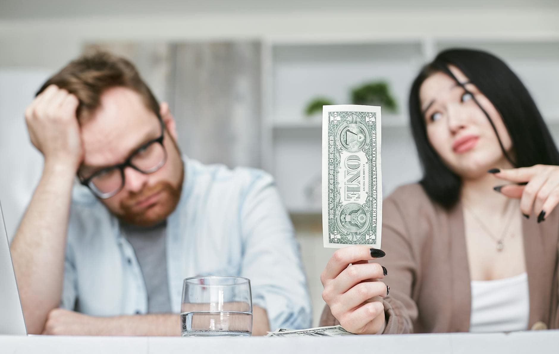 An adult interracial couple expressing concern about finances as they hold a one dollar bill indoors. - holiday financial stress relationships