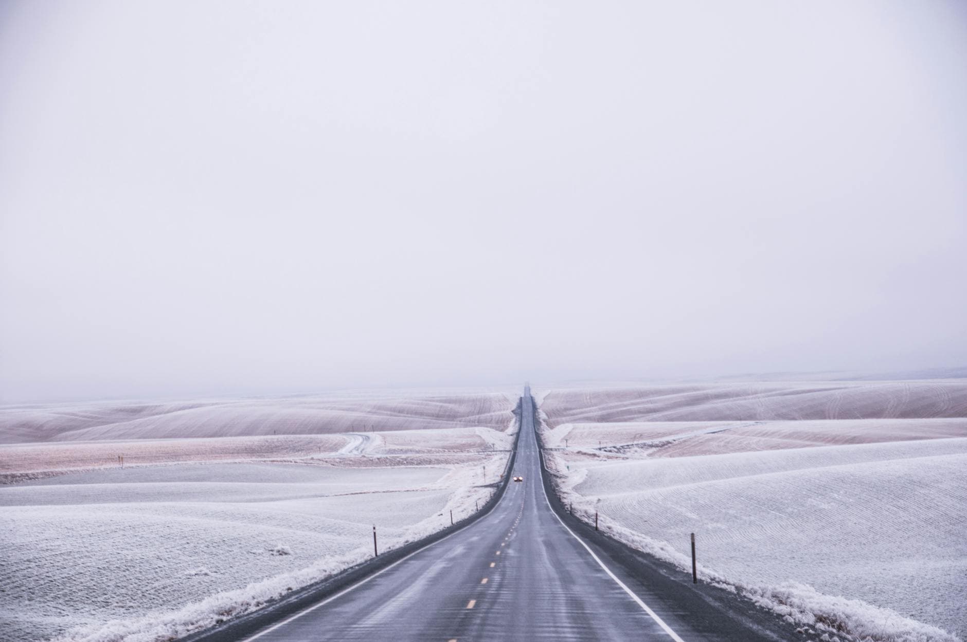 A lone road stretches through a vast snowy field, capturing winter's serene beauty. - long distance winter travel
