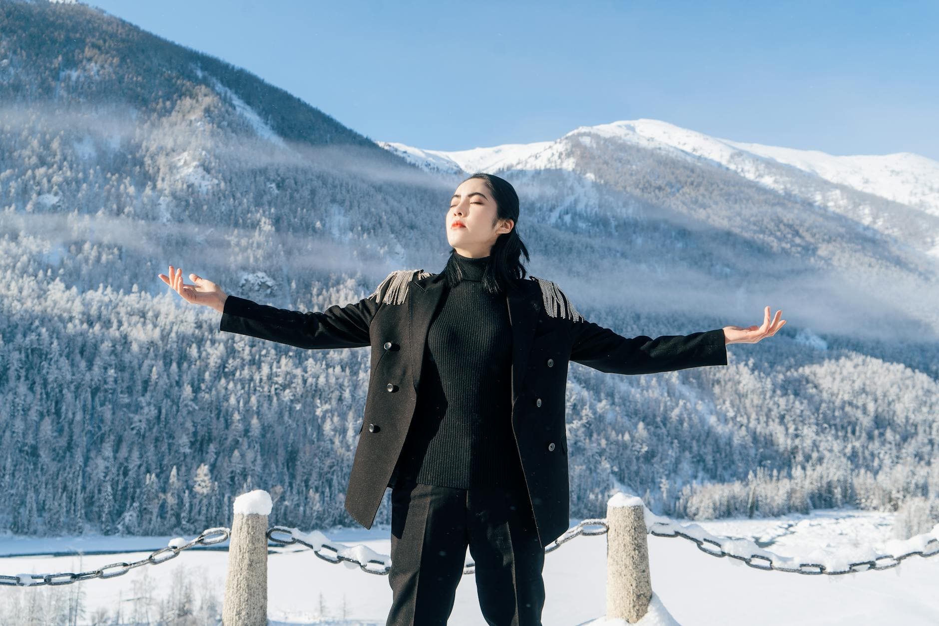 Woman in black outfit meditating amidst snowy mountains under a clear winter sky. - mindfulness for winter blues