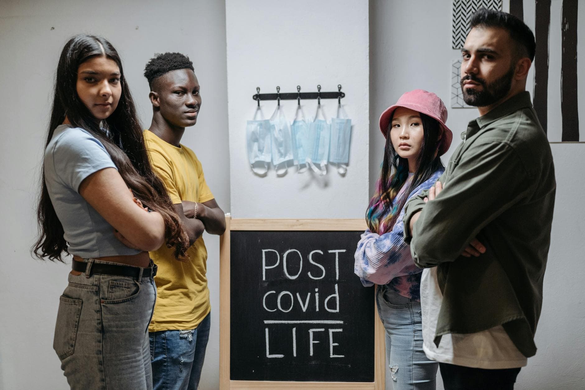 Diverse individuals standing in front of a chalkboard reading 'Post COVID Life' with hanging face masks. - rebuild intimacy after stress