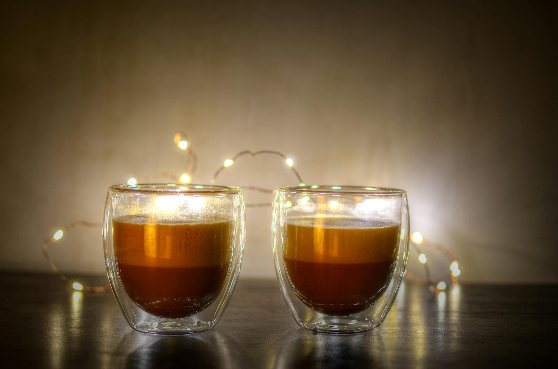 Two cappuccinos in double-walled glasses with festive lights. - winter mood boosting tips