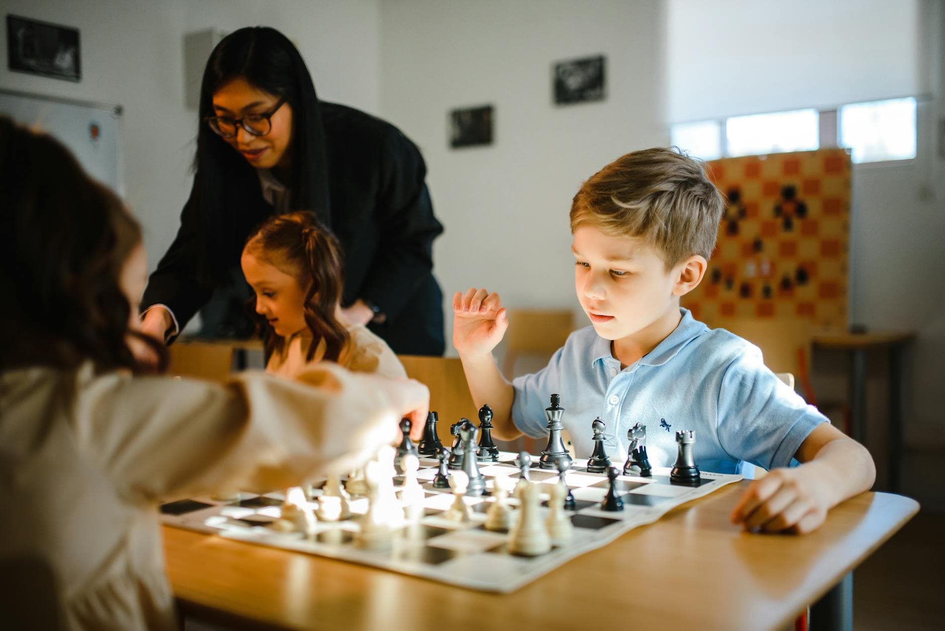 Young children playing chess under adult supervision in a classroom setting. - winter social skills for kids