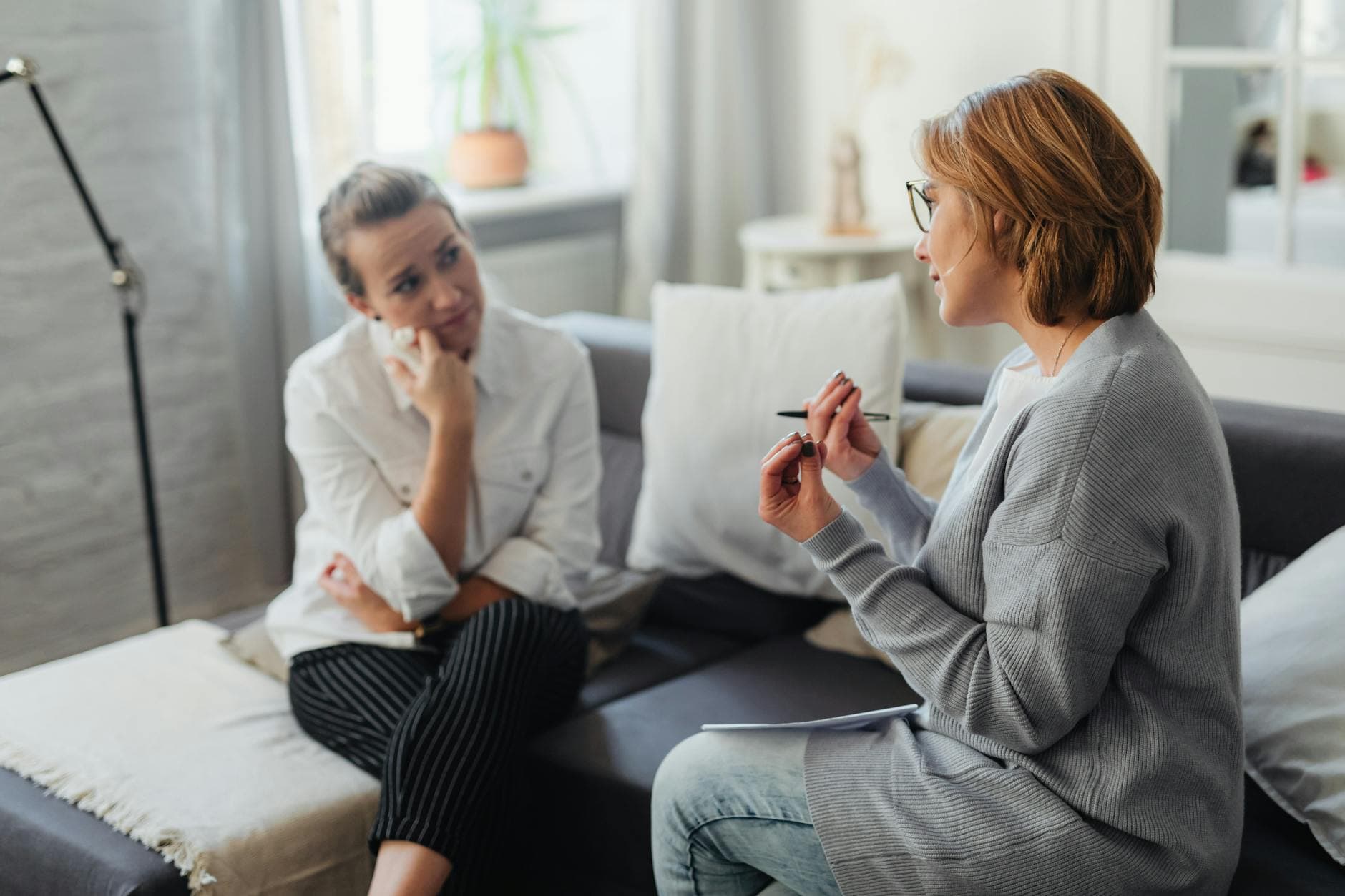 Two women, one being a therapist, engaging in a thoughtful conversation on a couch in a cozy room. - active listening definition