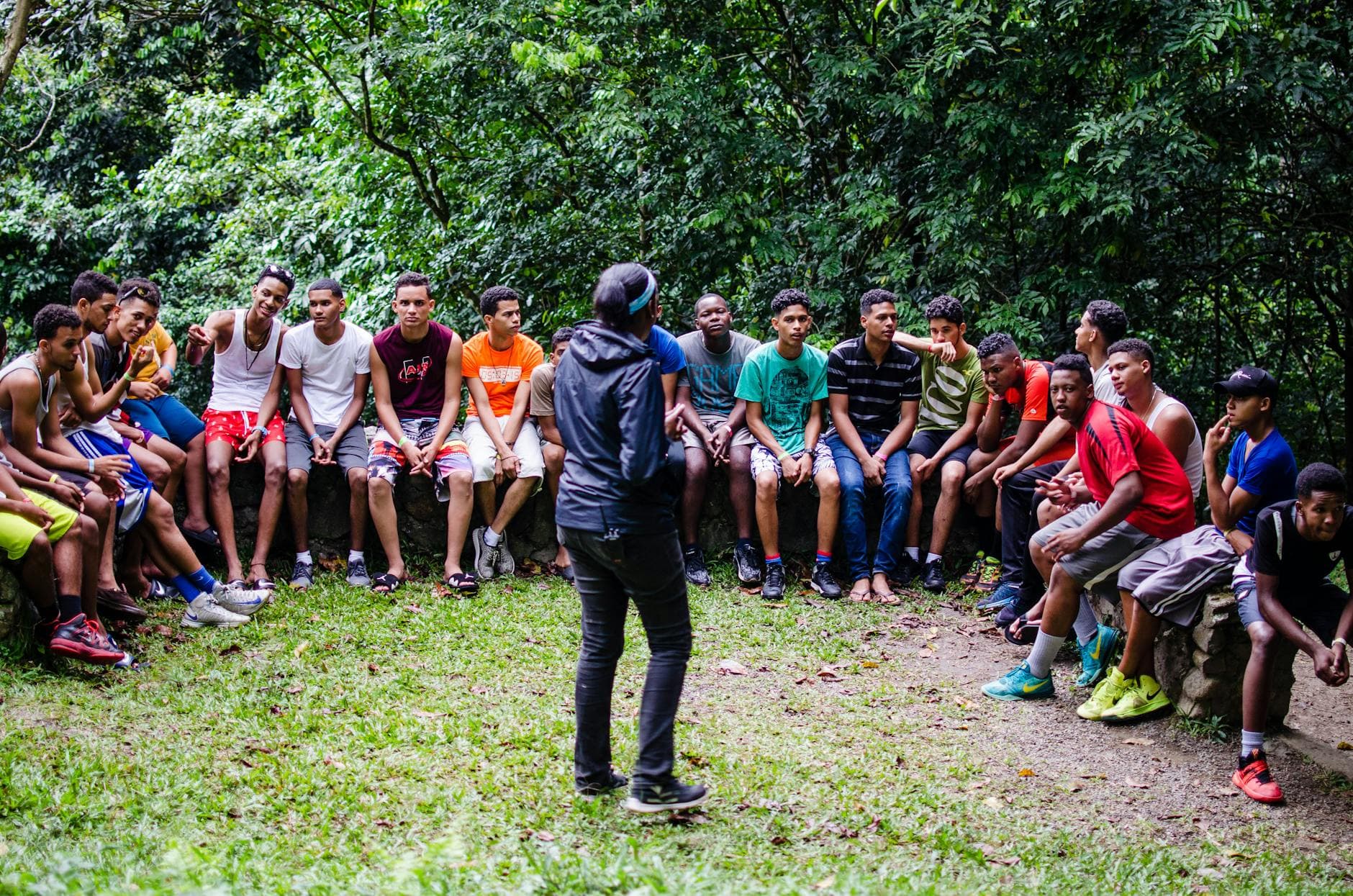A group of teenagers and adults listen attentively during an outdoor session in a green park. - active listening importance