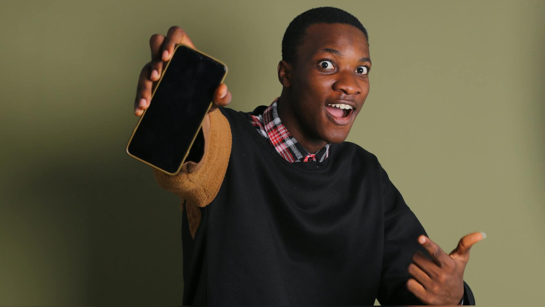 Happy young man showcasing a smartphone while enthusiastically pointing indoors. - address unspoken issues