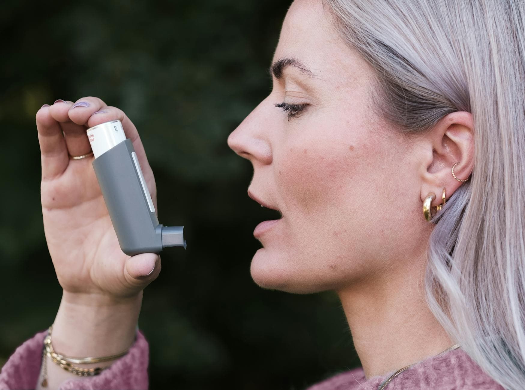 Close-up profile shot of a woman using an asthma inhaler outdoors, highlighting healthcare essentials. - allergy mental health
