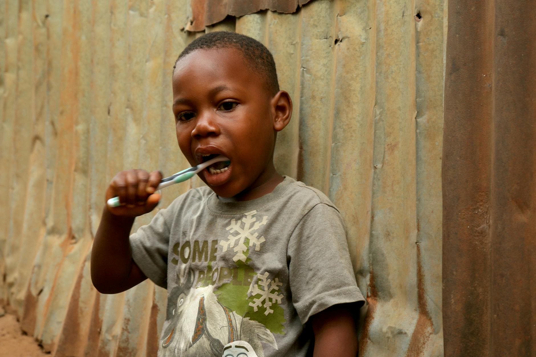 Young boy practicing oral hygiene outdoors near a corrugated metal wall in Freetown, Sierra Leone. - communication habits