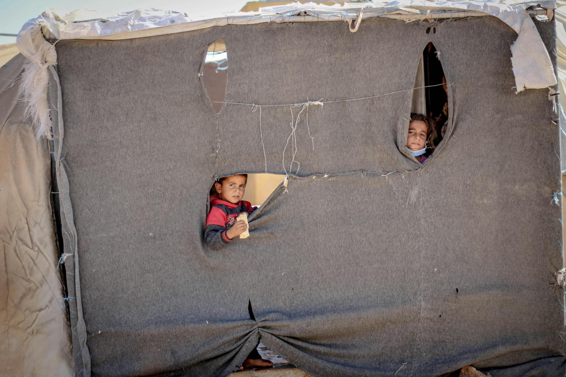 Children peeking through a makeshift tent in Idlib, highlighting resilience and hope. - emotional resilience children