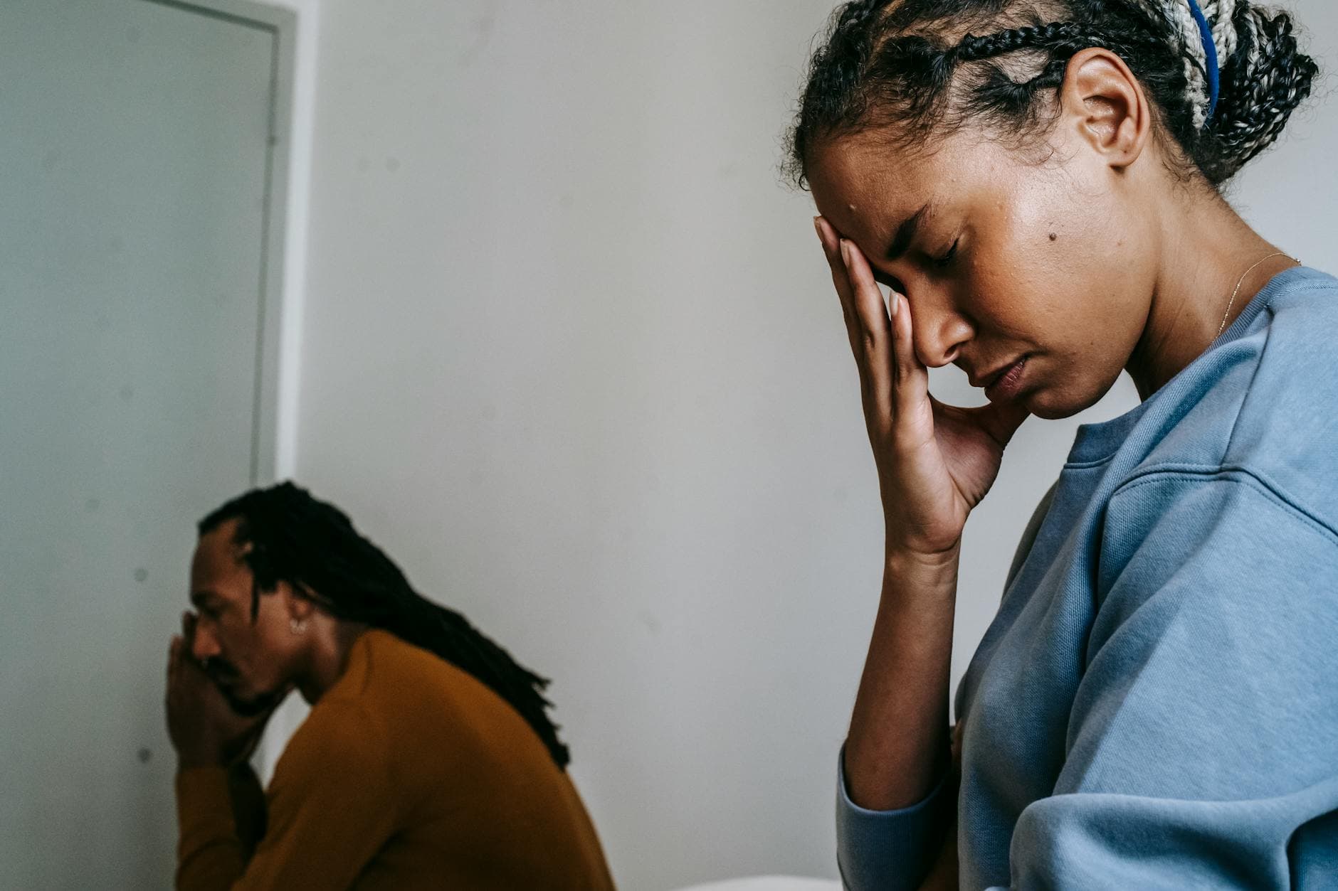 A young couple sits apart, visibly upset and deep in thought, in a home setting. - financial stress couple