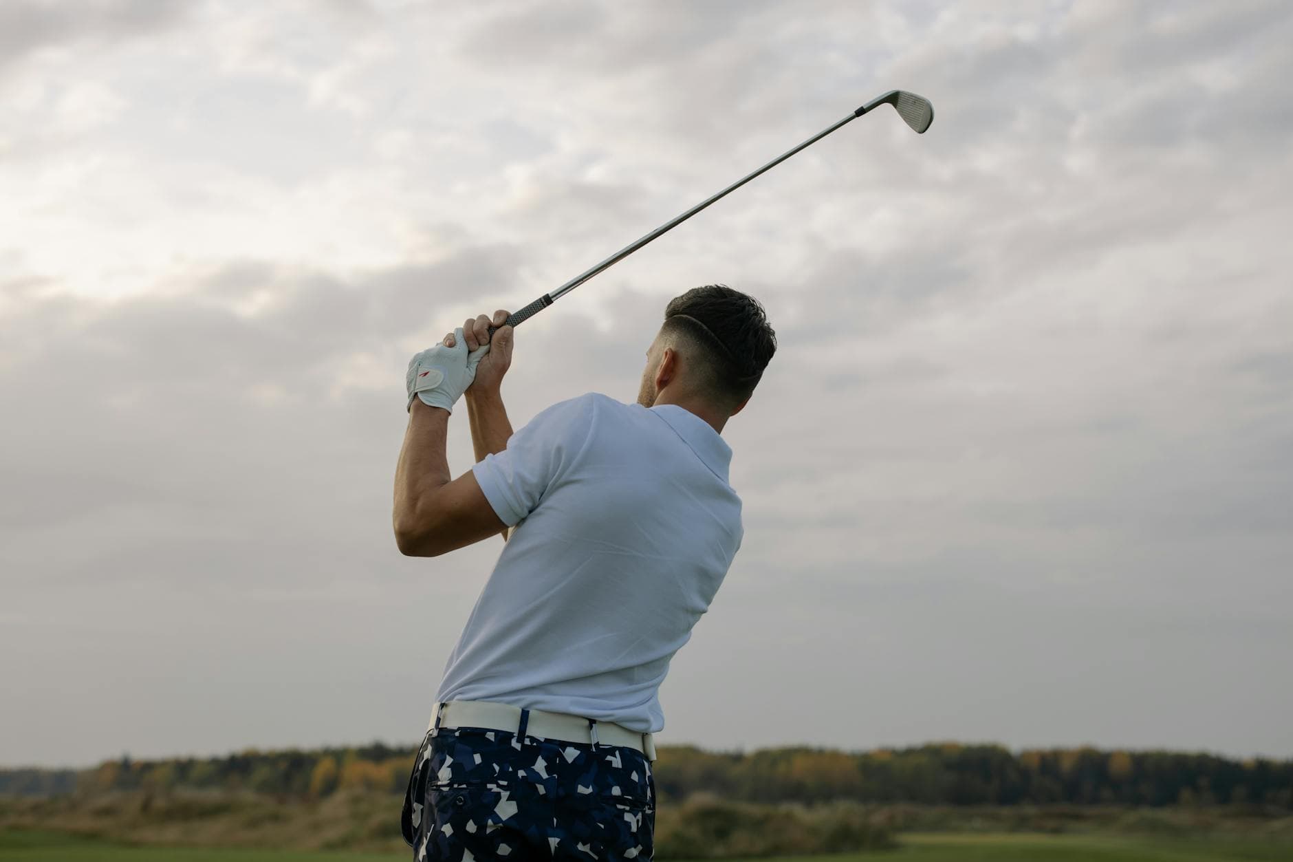 Back view of a golfer swinging a club outdoors on a cloudy day, showcasing the sport's precision and style. - find therapist mood swings