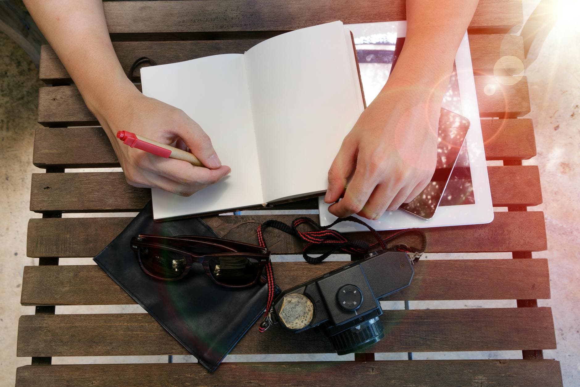 Top view of hands writing in notebook on wooden table with vintage camera and tablet. - journaling emotional release