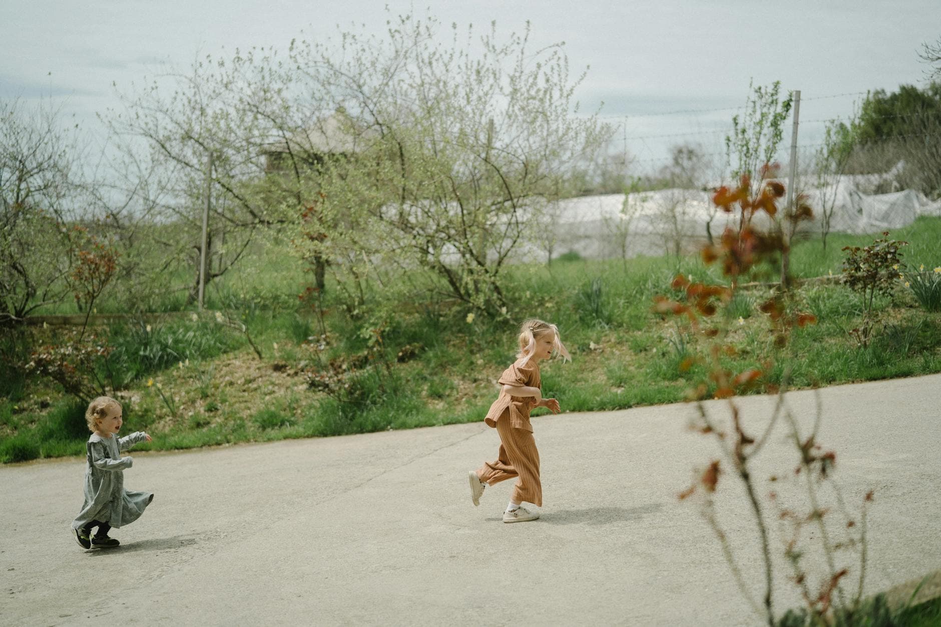 Two young children joyfully running in a green outdoor setting, capturing the essence of playful freedom. - kids spring gardening