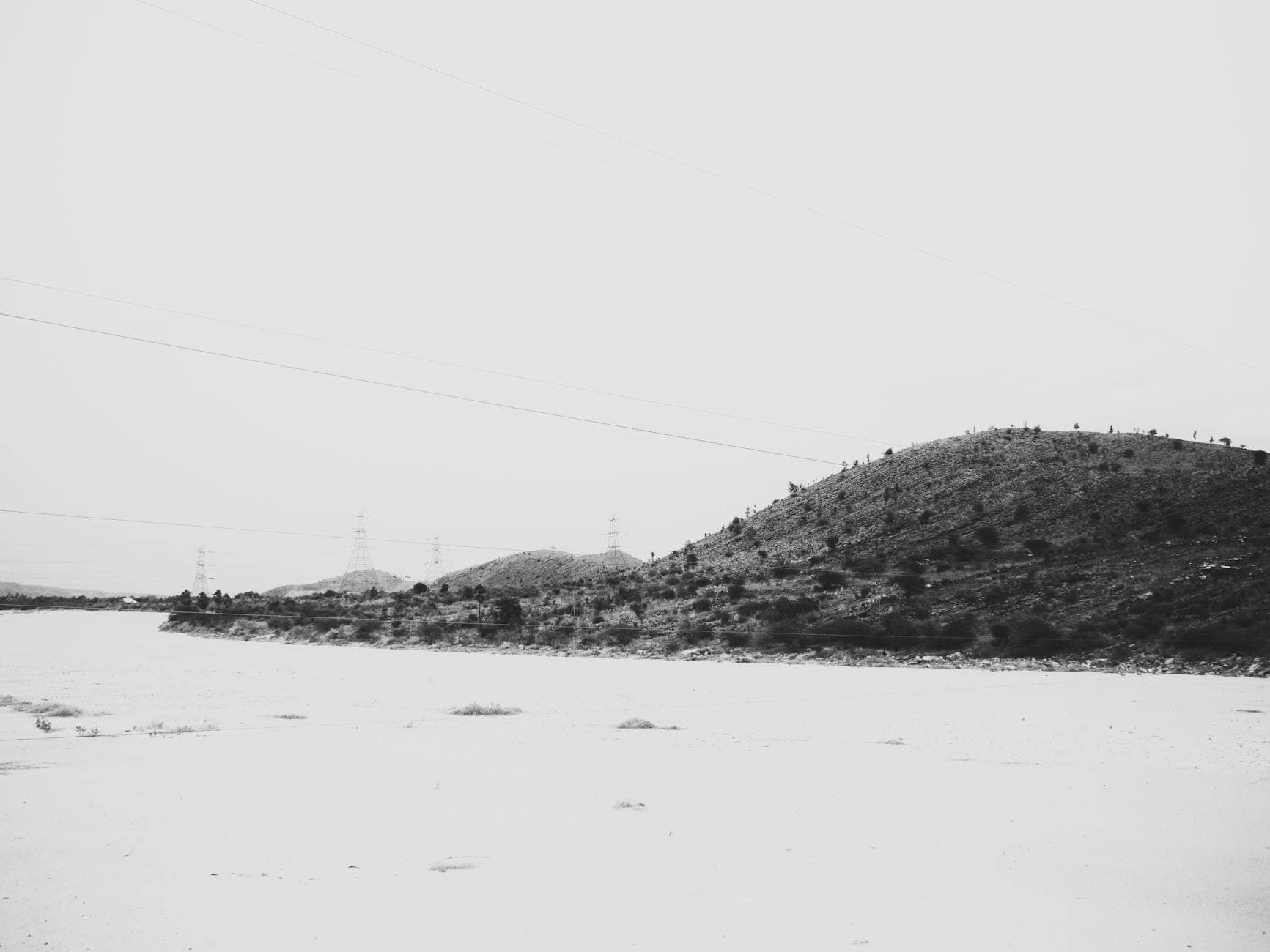 A monochromatic view of barren hills with transmission towers under an overcast sky, evoking a sense of solitude. - lack of empathy