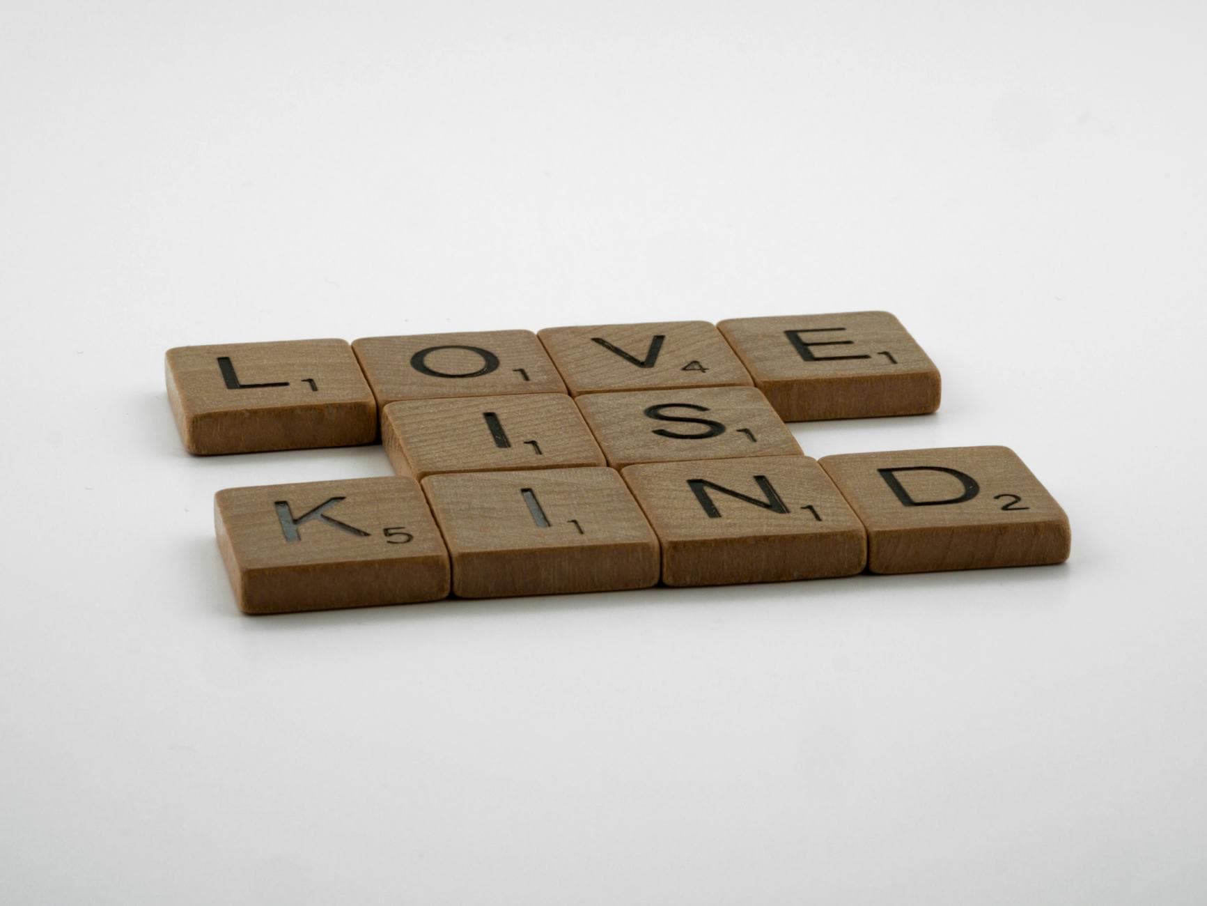 Wooden Scrabble tiles arranged to say 'Love is Kind' on a plain background. - love languages explained