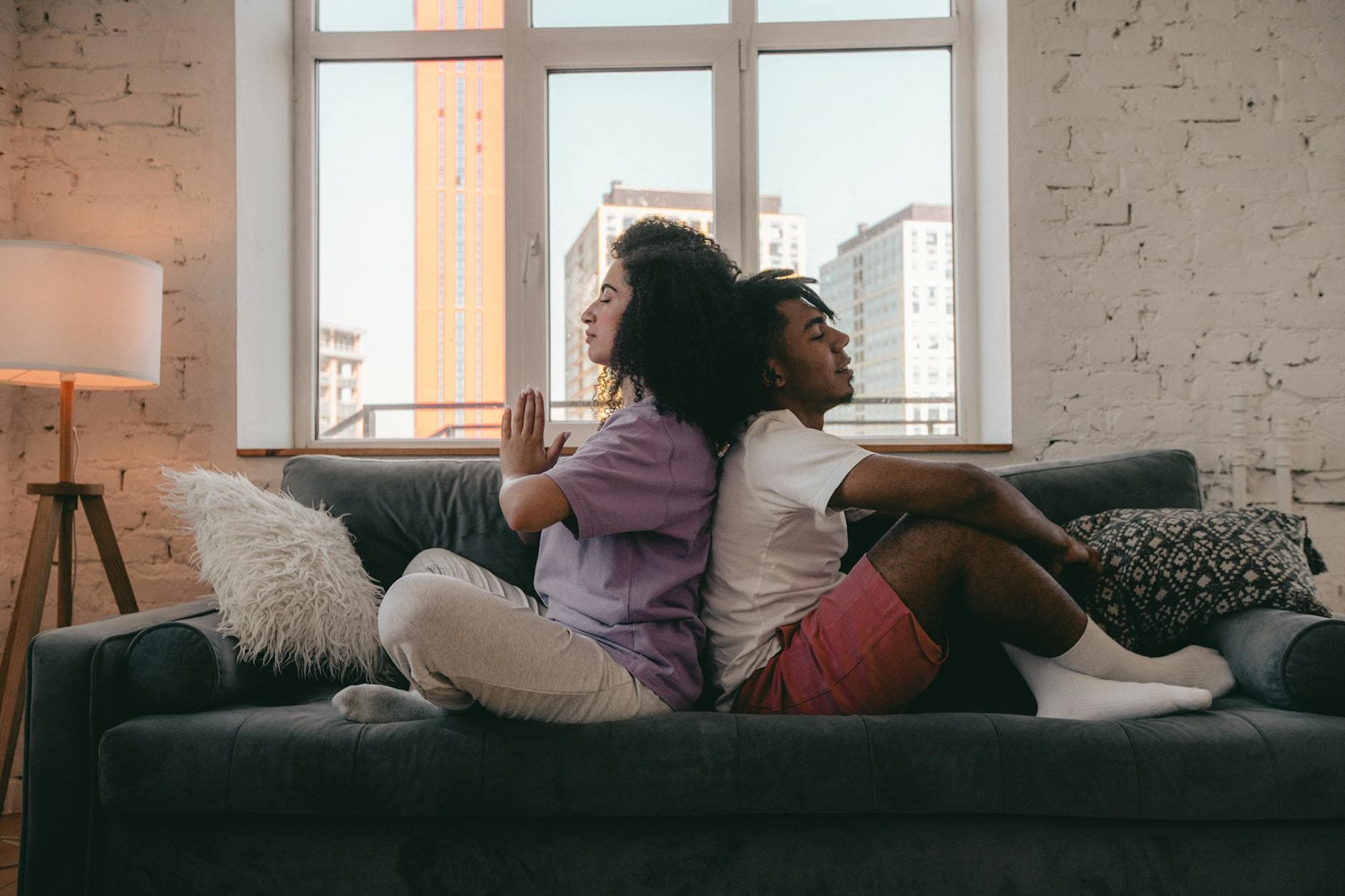 Interracial couple practicing meditation back-to-back on a couch. Calm and peaceful ambiance. - marital resentment