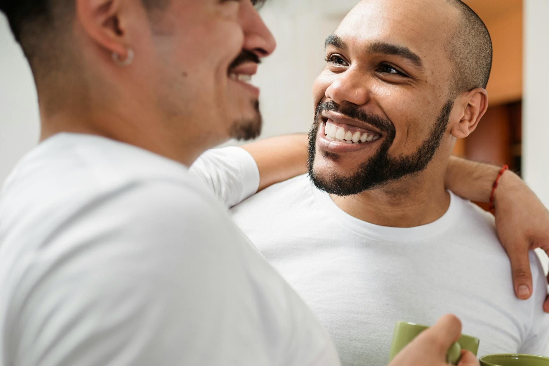 A happy couple shares a moment of joy indoors, embracing and smiling while holding coffee mugs. - marriage advice men