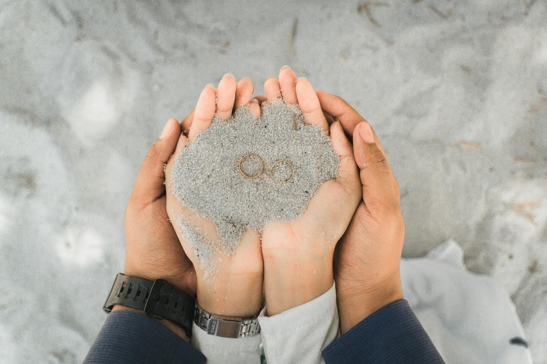 Close-up of a couple holding wedding rings in sand, symbolizing love and union. - marriage advice shower