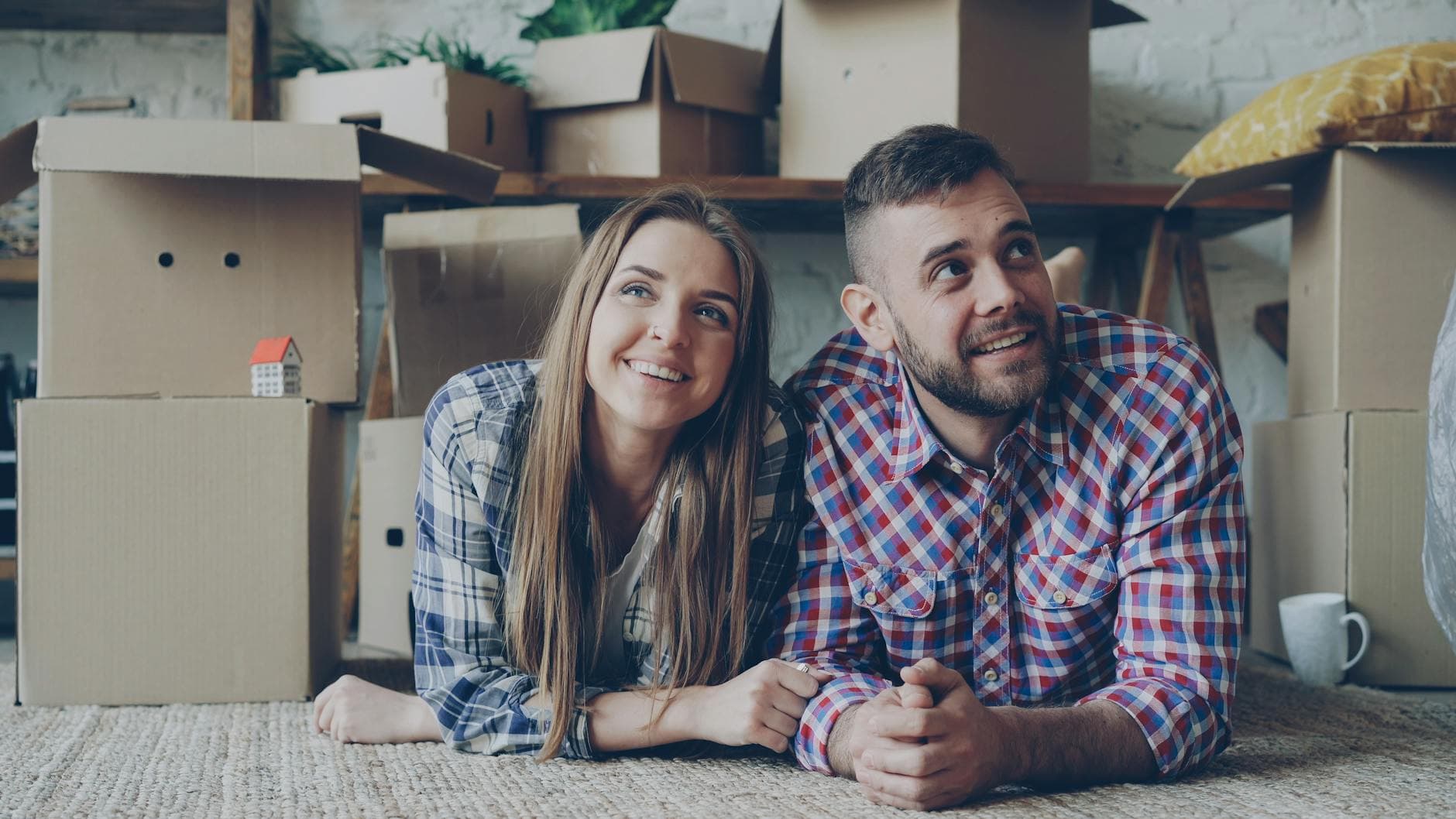 Happy couple lying on carpet surrounded by moving boxes in their new home. - new relationship growth