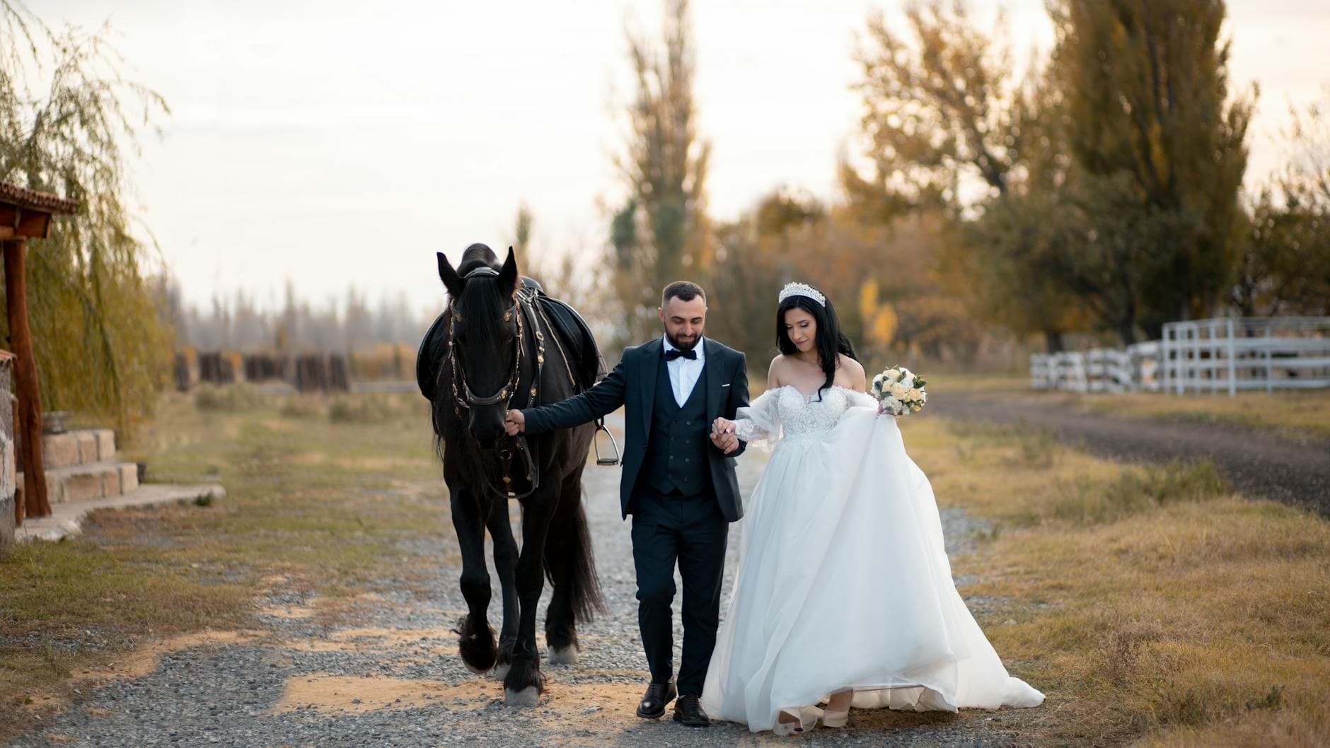 Bride and groom walking a black horse in rural setting, elegant wedding attire. - newlywed marriage advice