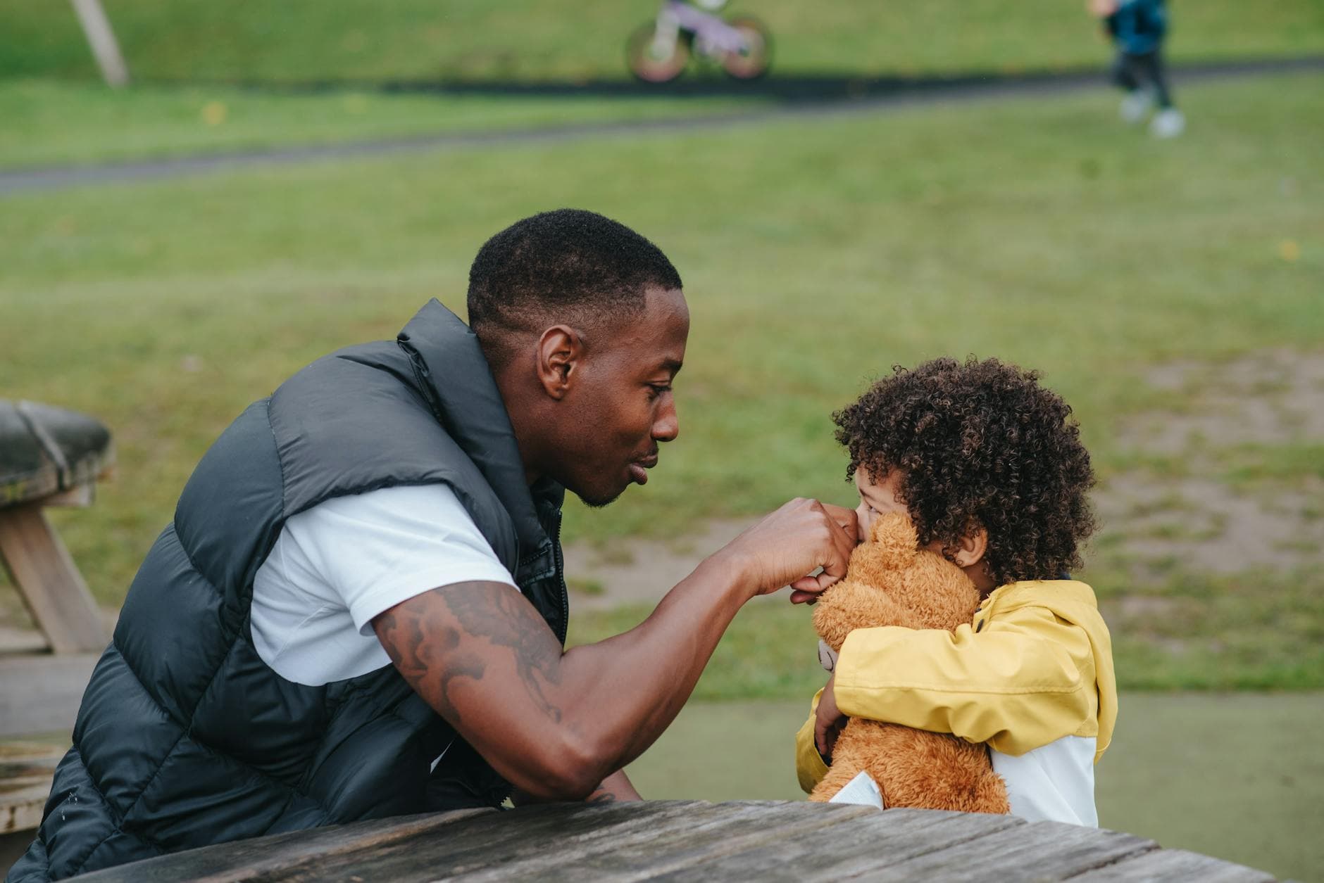 A heartwarming moment of father and son bonding at the park with a teddy bear. - preschool emotional intelligence