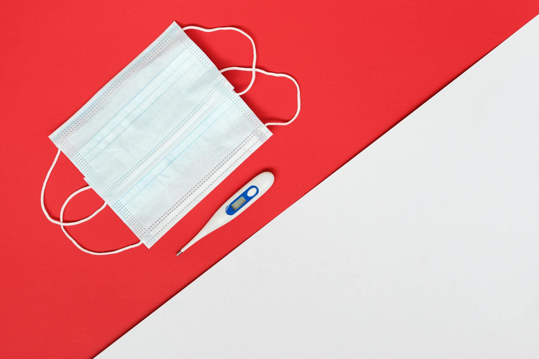 Flat lay of a face mask and digital thermometer on red and white background. - prevent spring s.a.d.