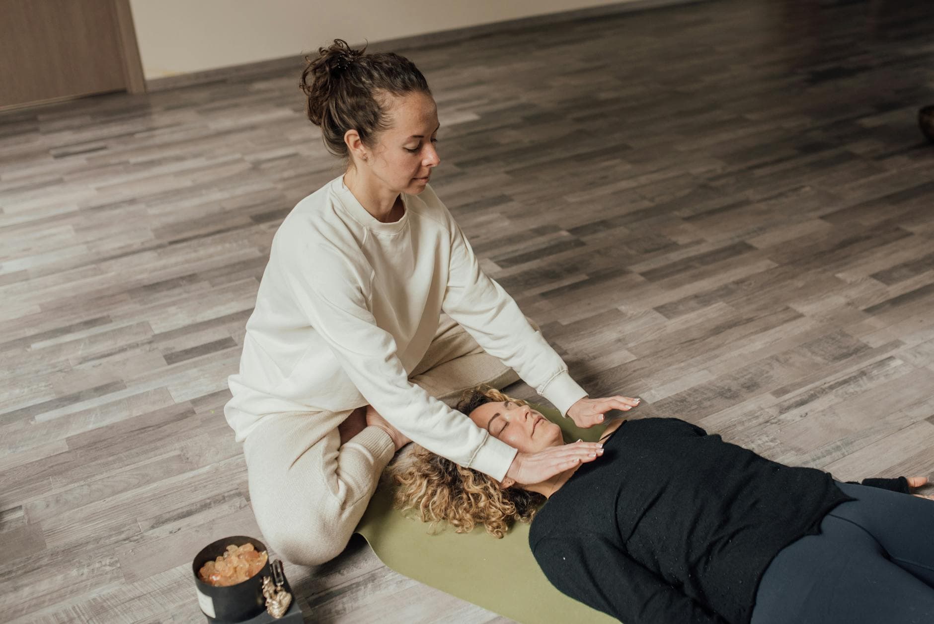Woman practicing Reiki healing therapy on another woman lying indoors on a yoga mat. - relationship healing