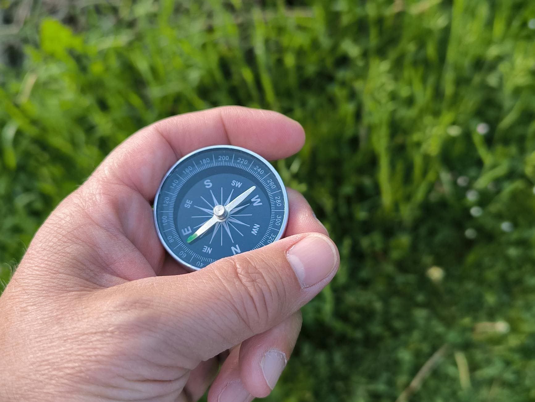 Close-up of a hand holding a compass with a green field in the background. - self-compassion practices