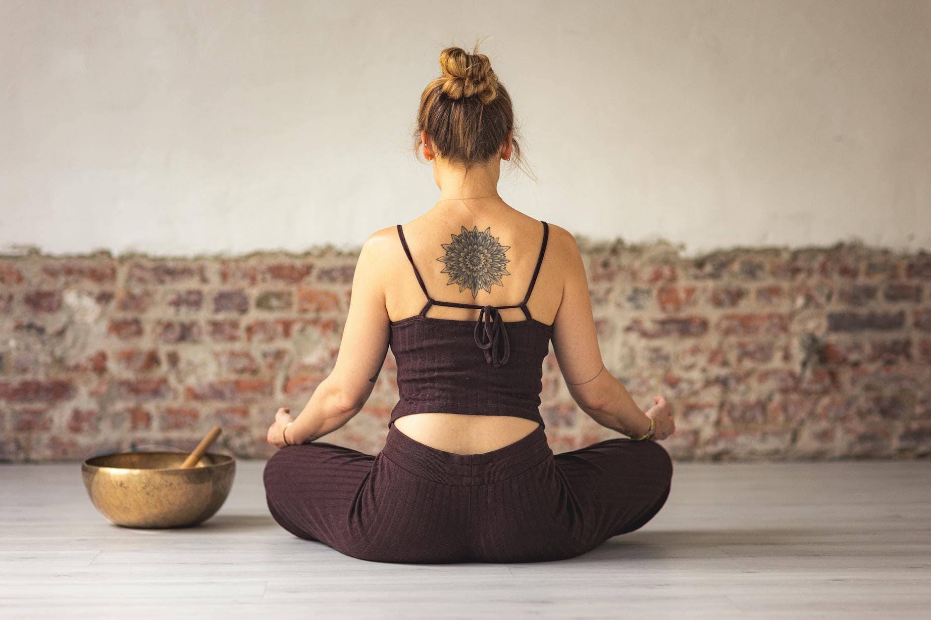 Woman meditating indoors with a tattoo on her back, embracing peace and zen. - self compassion practices