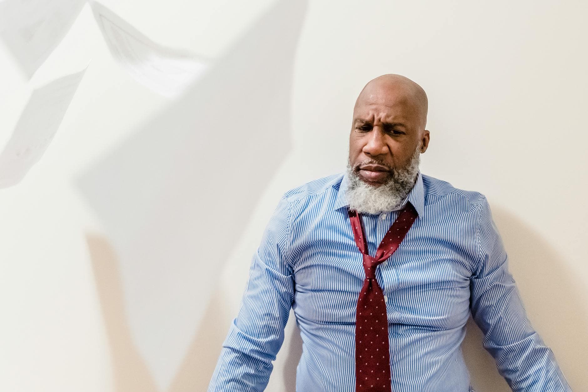 A man in a shirt and tie looks frustrated as papers fall around him indoors. - spring anxiety adults
