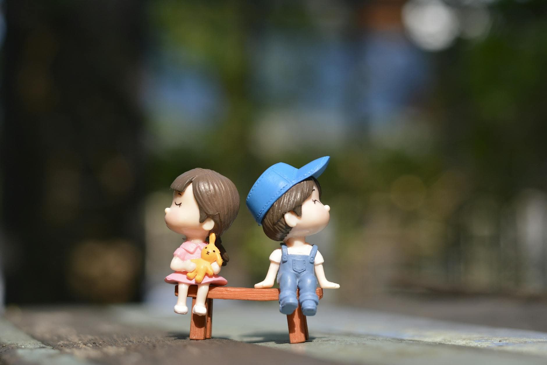 Adorable figurines of a boy and girl sit on a bench, bathed in summer sunlight. - spring break kids