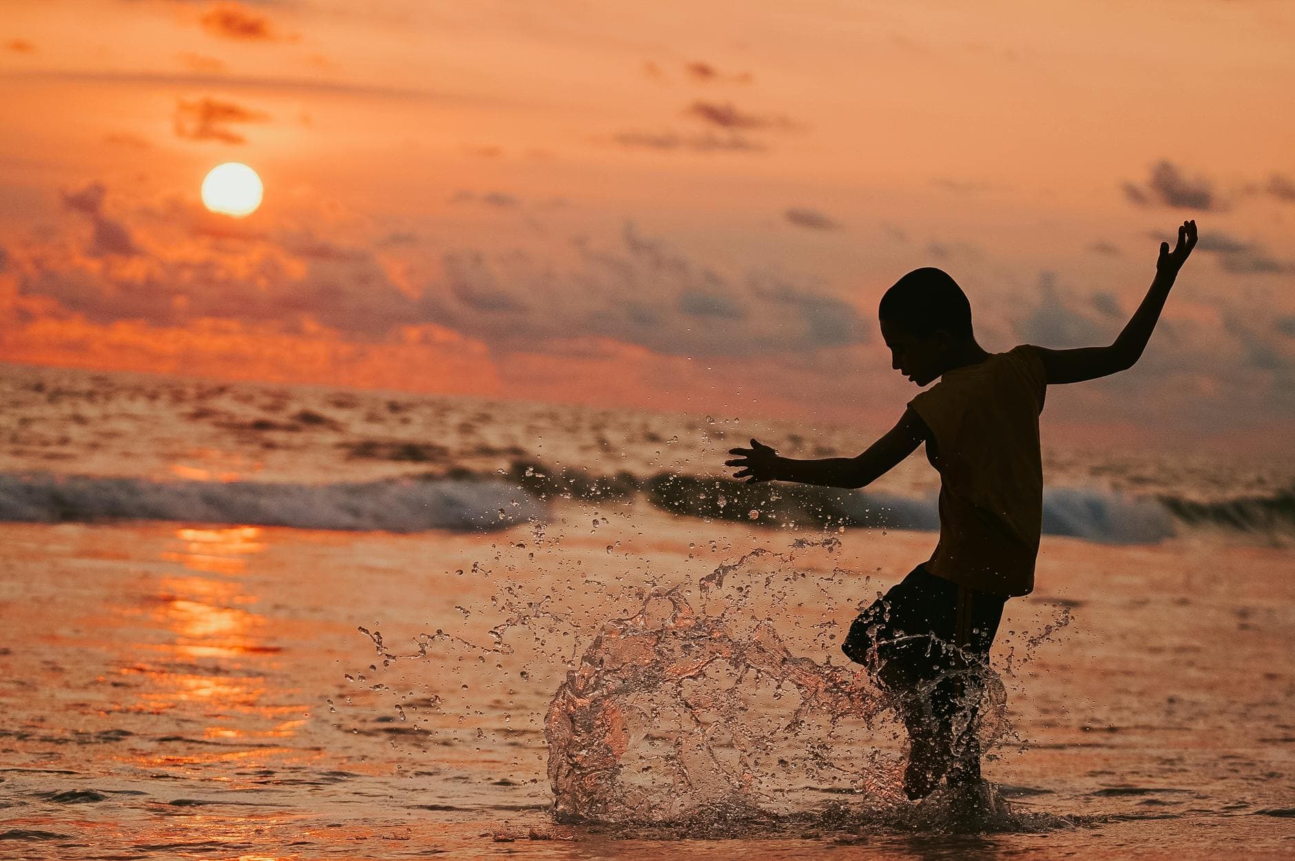 A child joyfully splashing in the ocean waves during a vibrant sunset, capturing pure happiness and freedom. - spring child energy