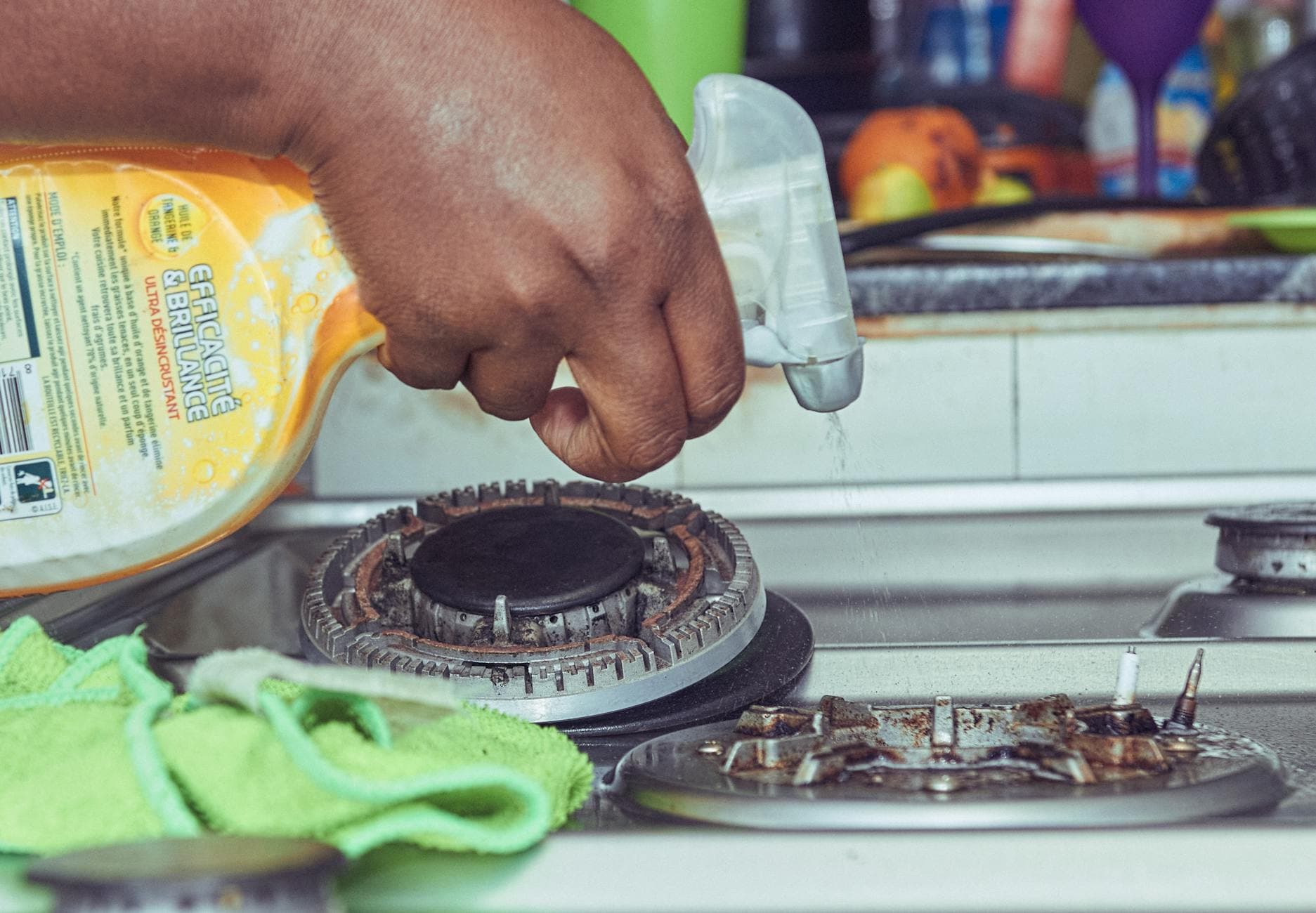 A detailed view of a hand cleaning a stovetop using a spray bottle and cloth. - spring chore division