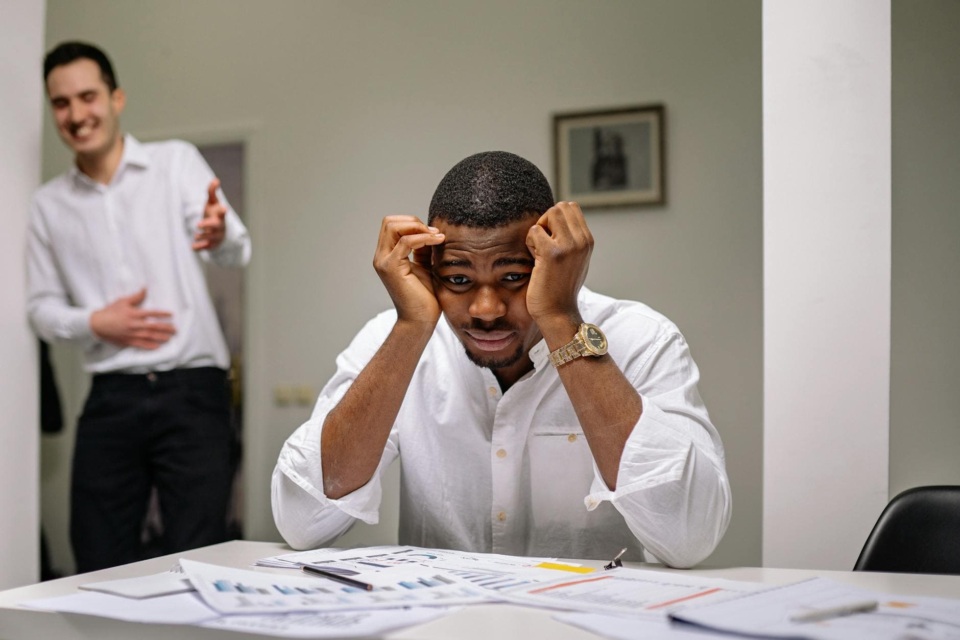 Tensed businessman at desk while coworker is laughing. Office stress concept. - spring stress families