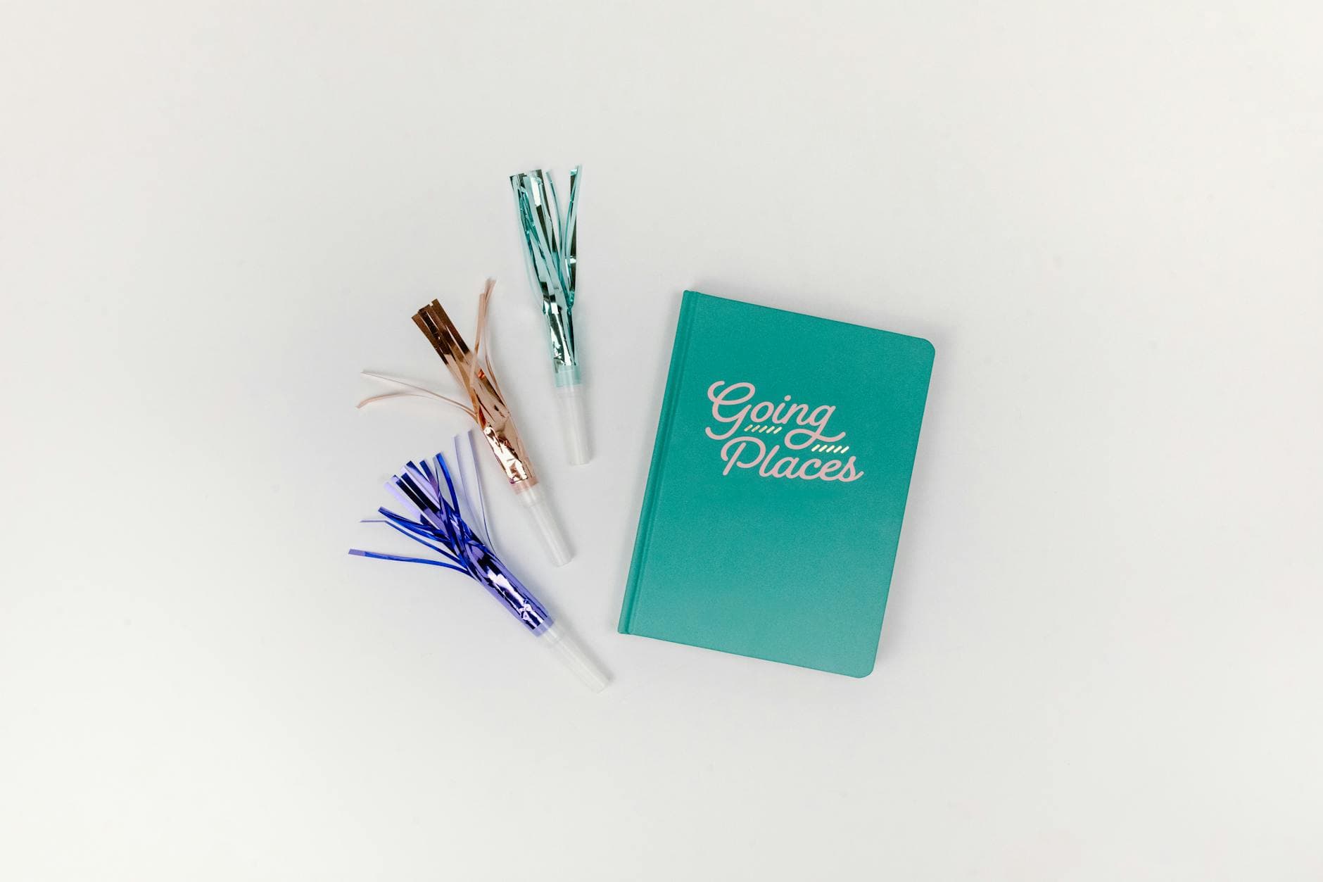 A teal journal titled 'Going Places' paired with colorful party blowers on a white background. - therapeutic journaling prompts