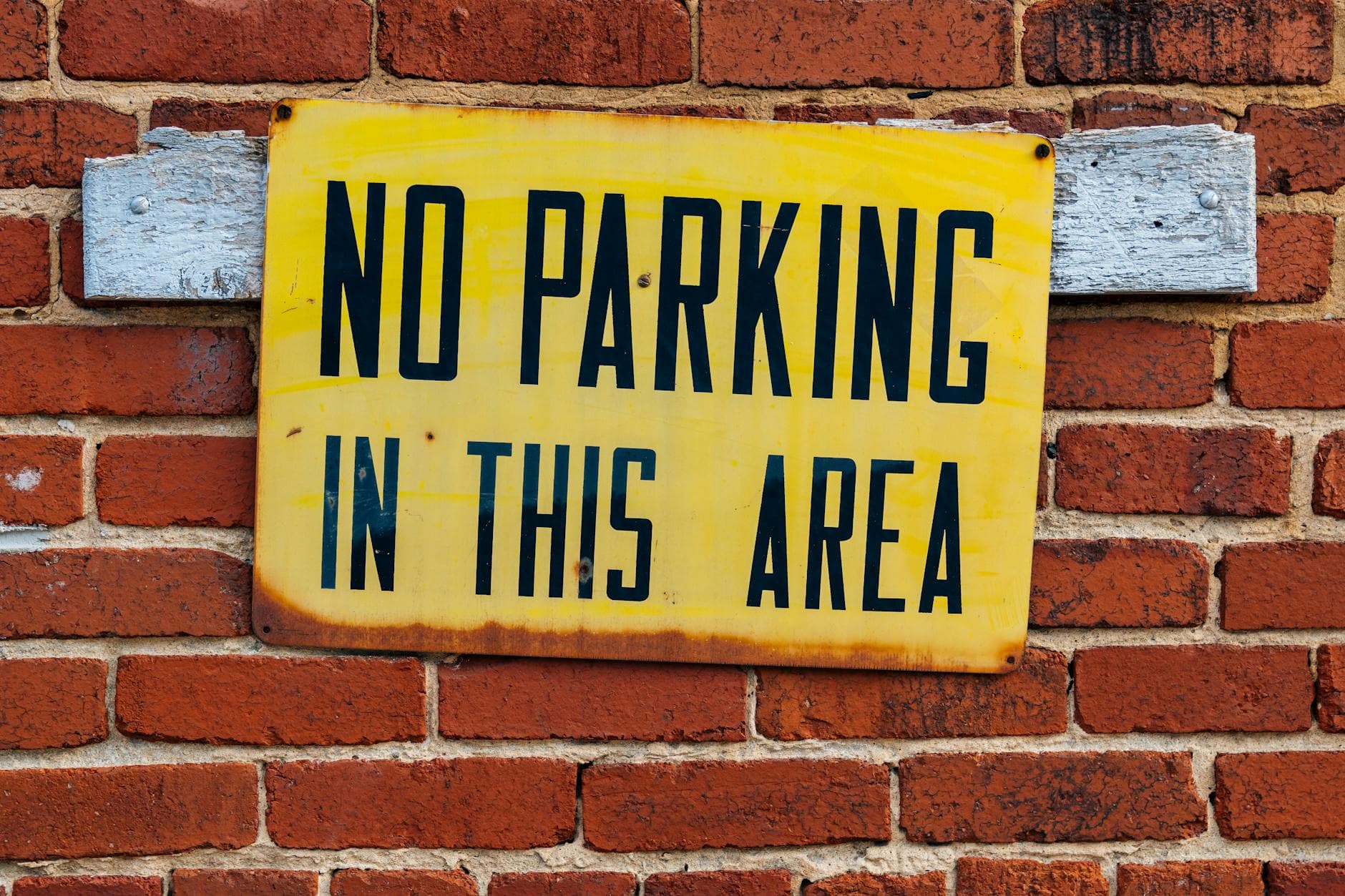 Bright yellow no parking sign attached to a red brick wall. - toddler emotional regulation