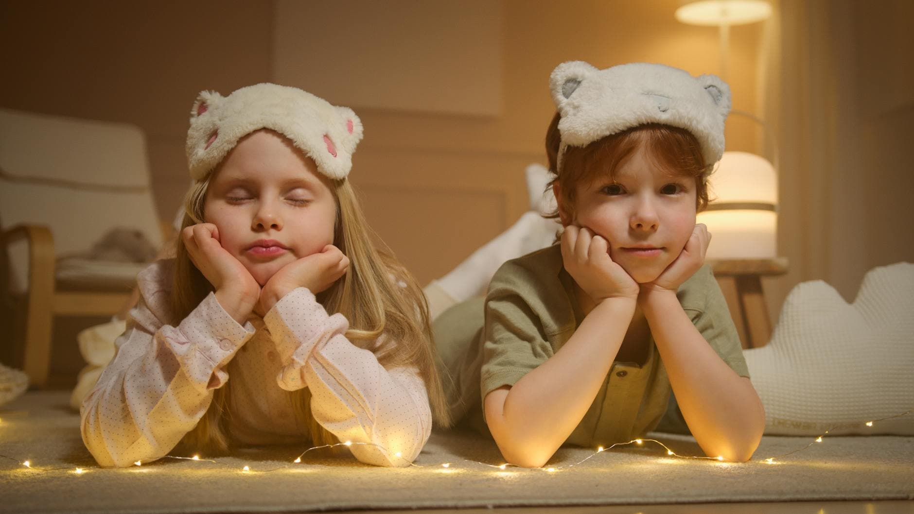 Two children wearing cute sleep masks enjoy a cozy indoor setting with soft lighting. - winter sleep children