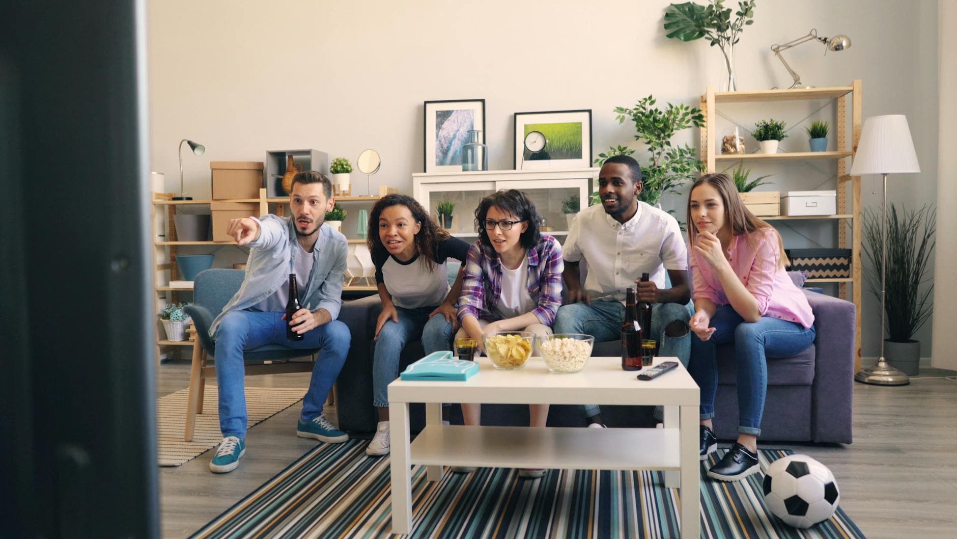 Diverse group of friends cheering for a sports game in a cozy living room setup. - anger management tv shows