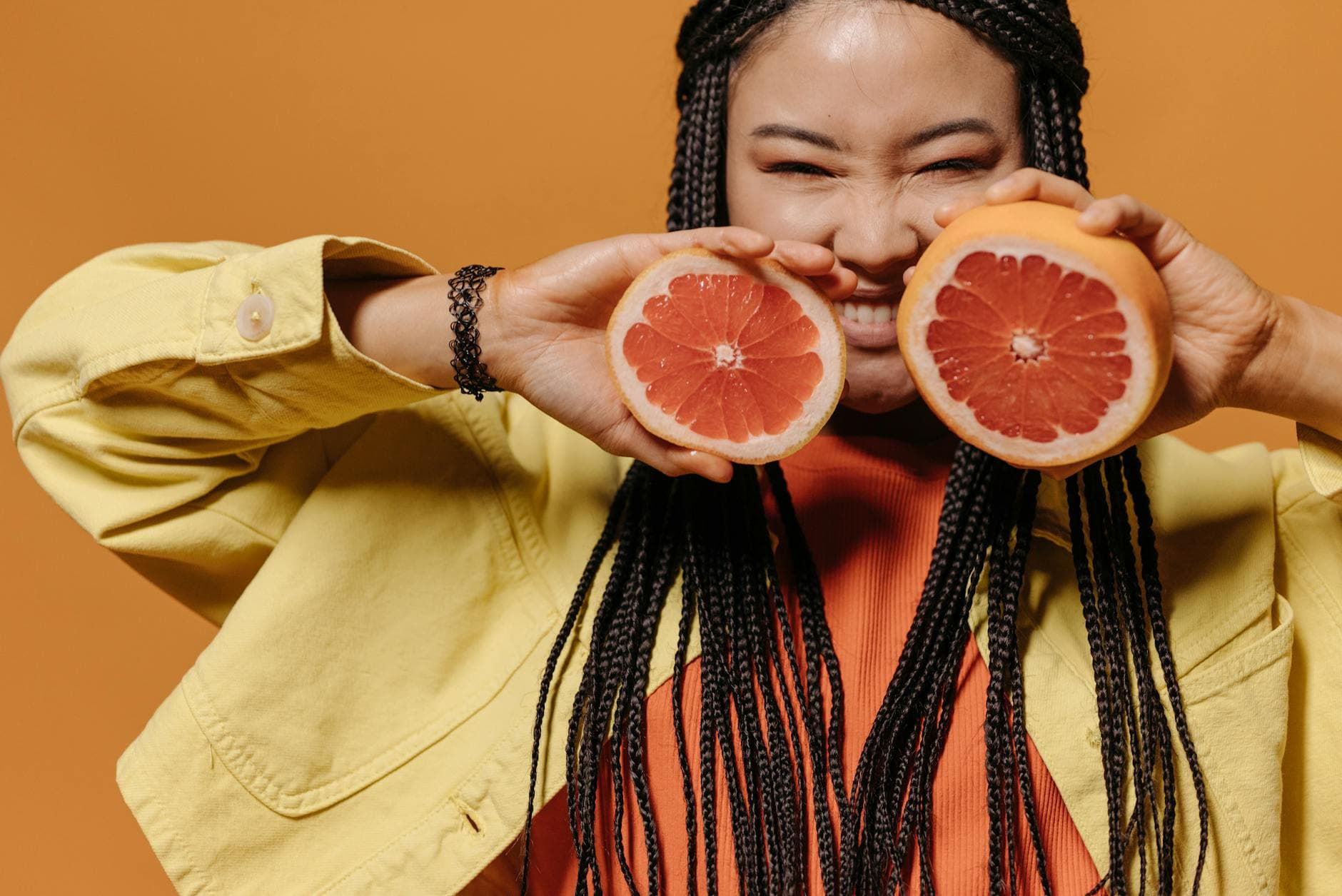A fashionable woman with braided hair holding grapefruits against a vibrant orange background. - boost mood naturally