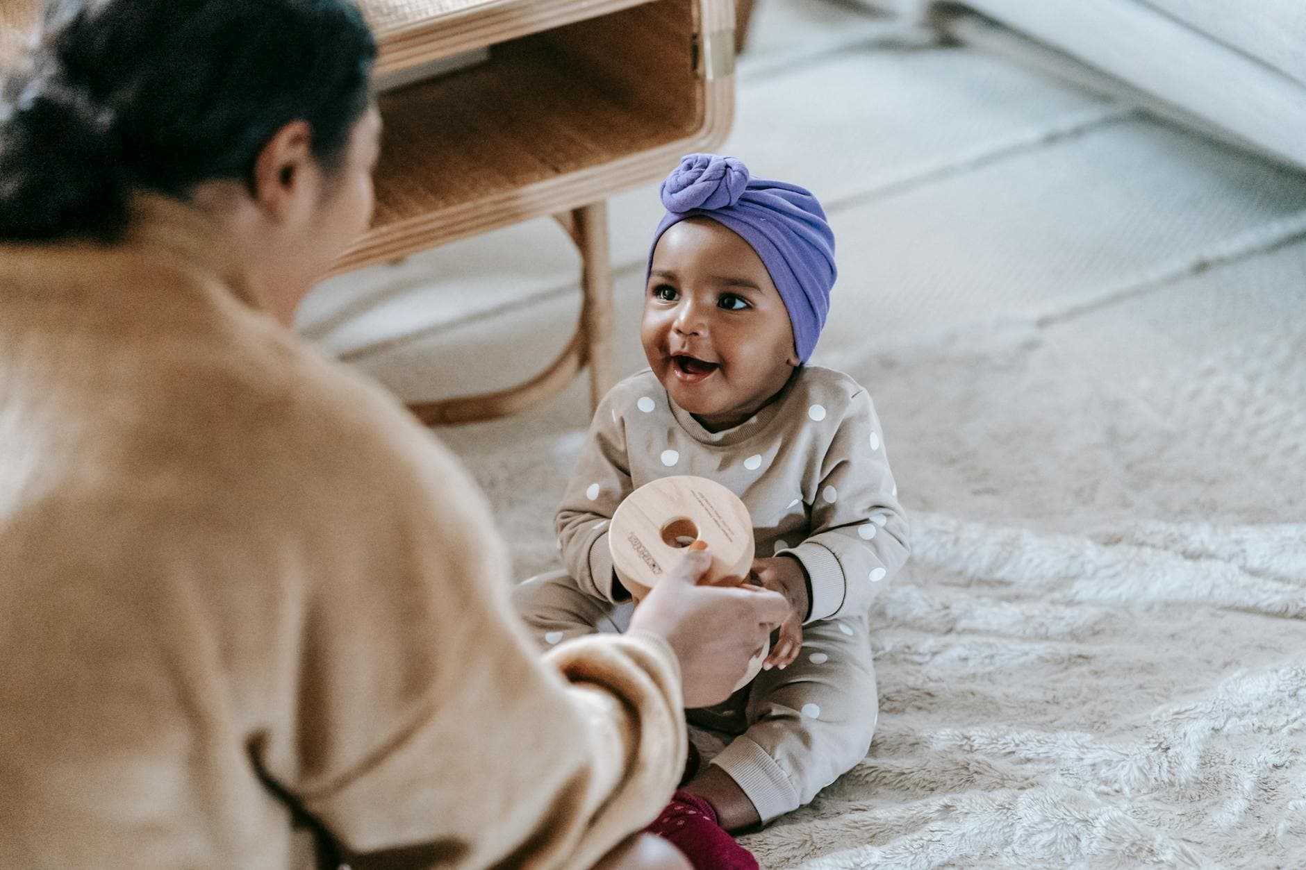 Anonymous African American mother sitting on floor near little black toddler with wooden toy while spending time in living room at home - child development milestones