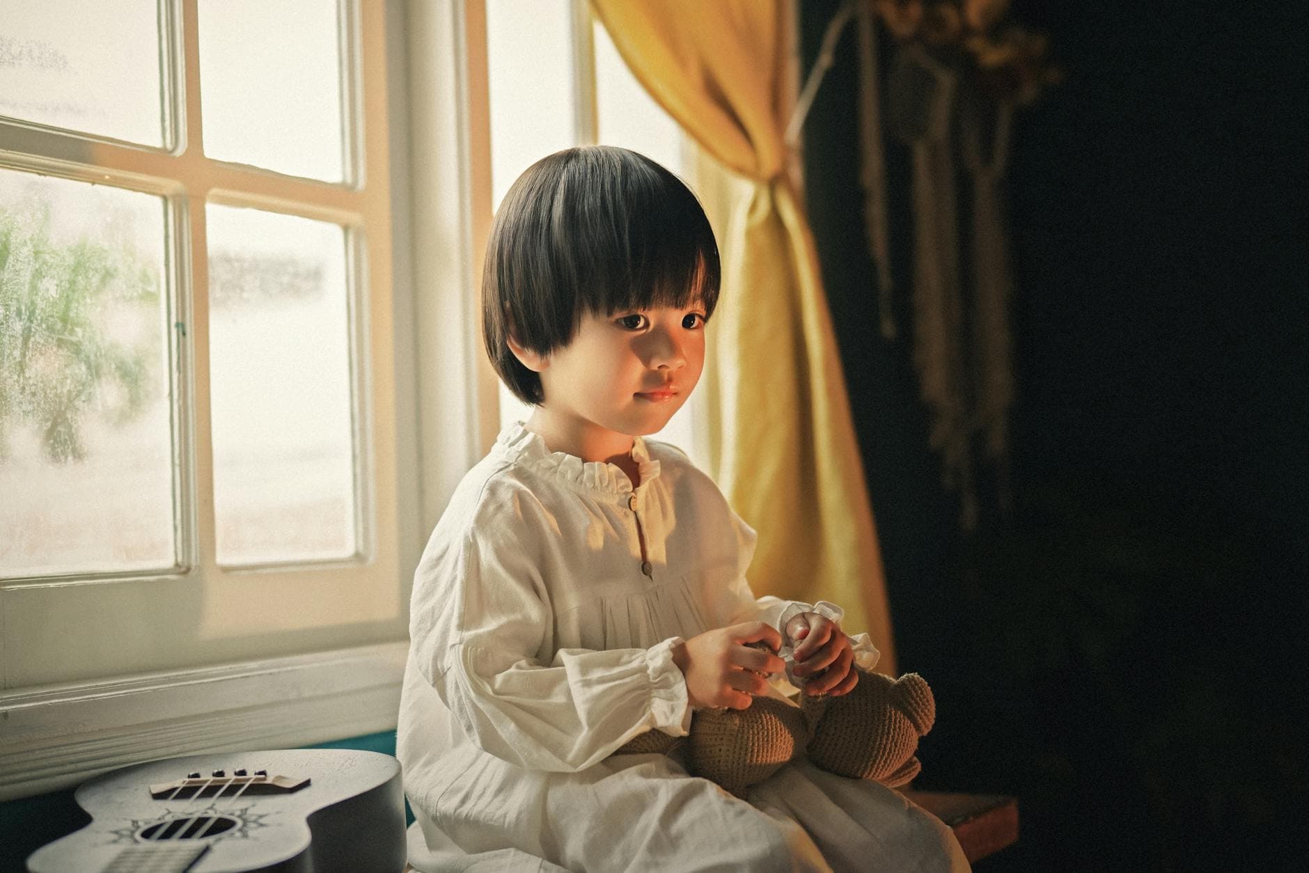 A serene portrait of a child inside, holding a teddy bear by a window. - child emotional changes