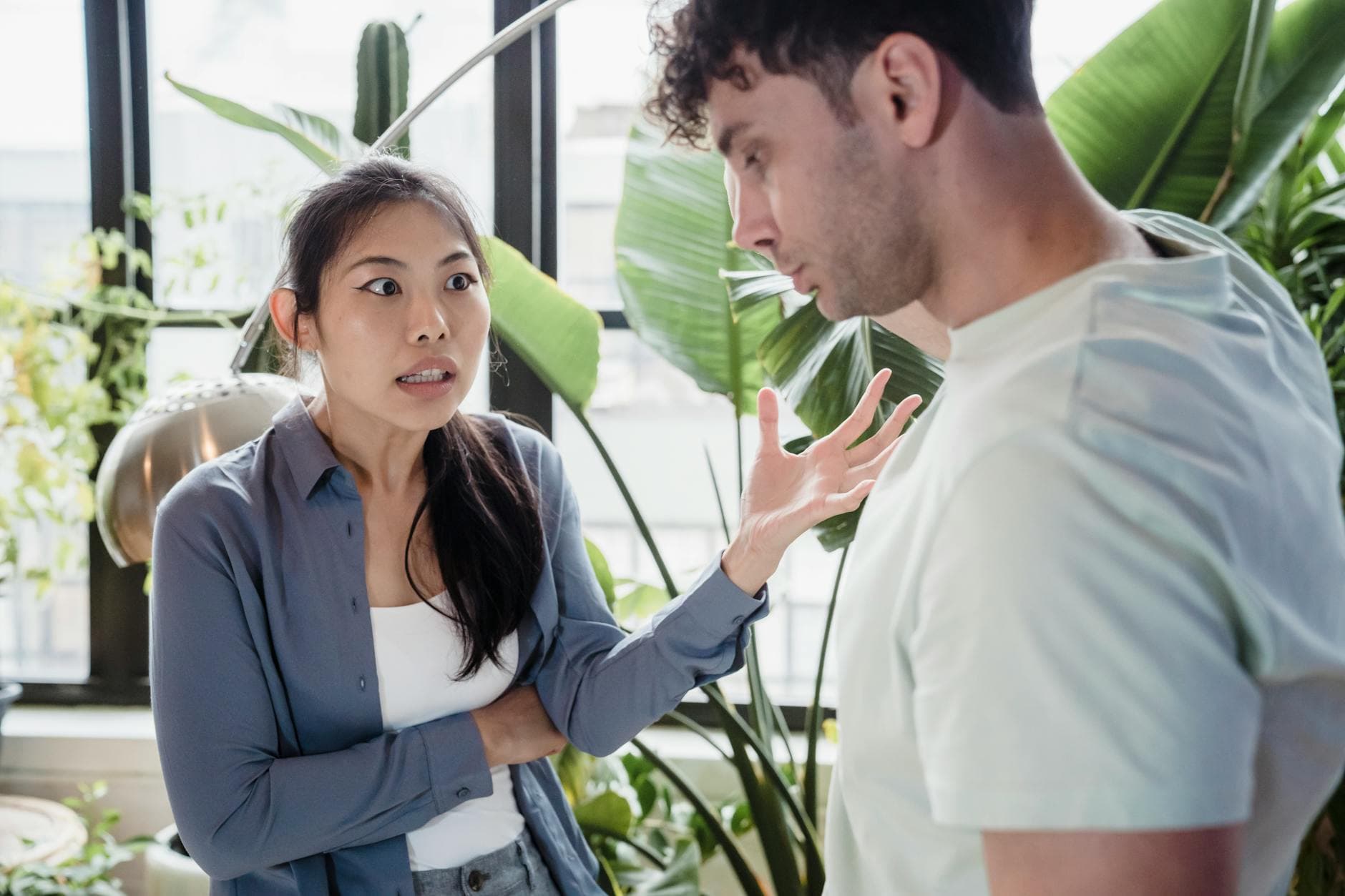 A couple engaged in a heated discussion indoors surrounded by plants, expressing emotions. - conflict meaning