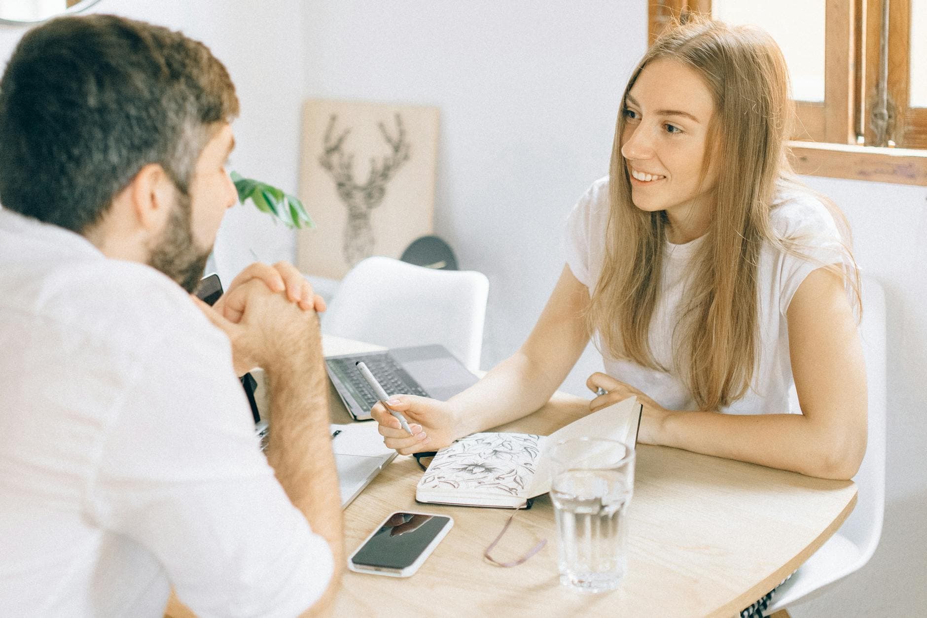 A smiling woman and man having a friendly discussion at a table with a notebook and laptop. - effective communication skills
