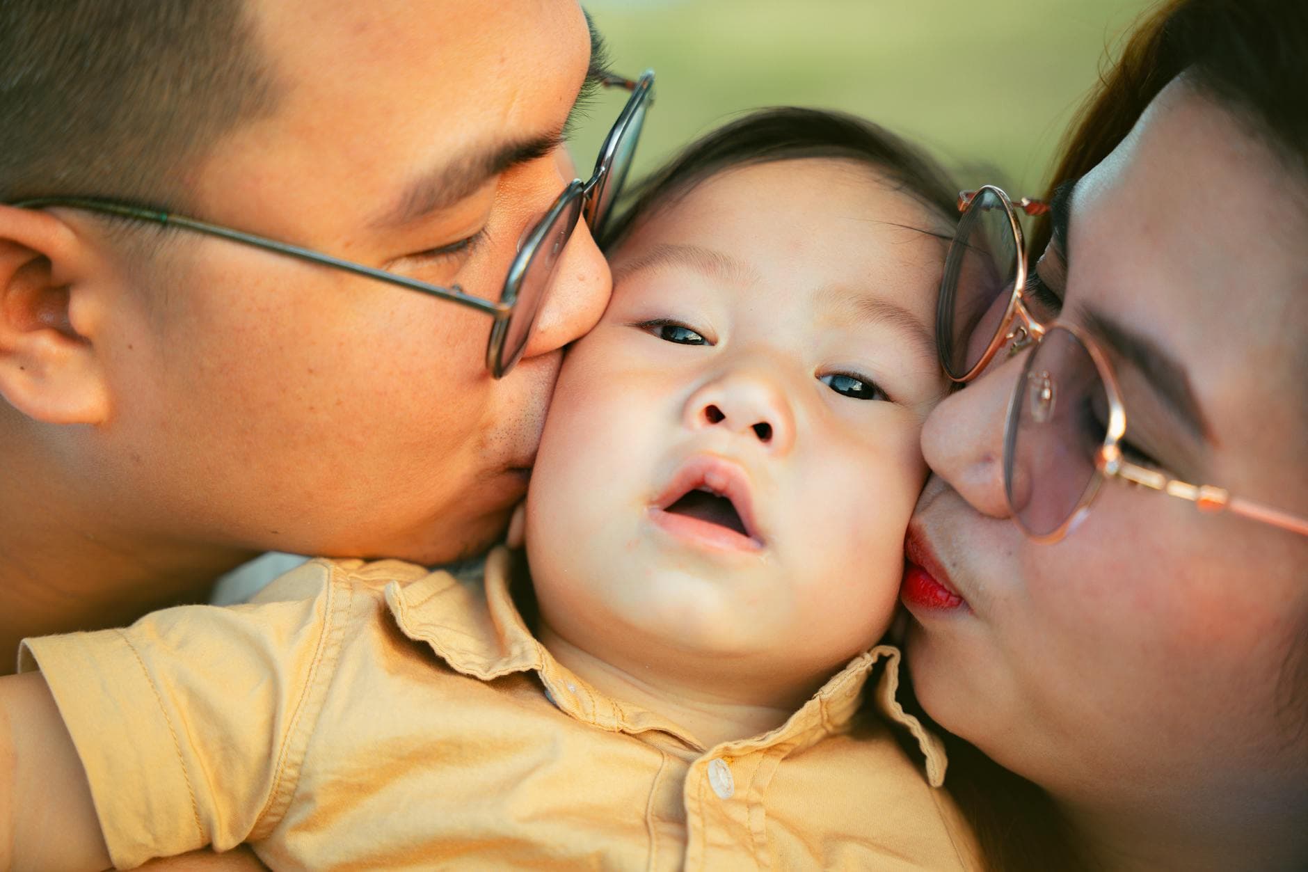 Close-up of affectionate parents kissing their baby, capturing a heartwarming family moment. - express needs family