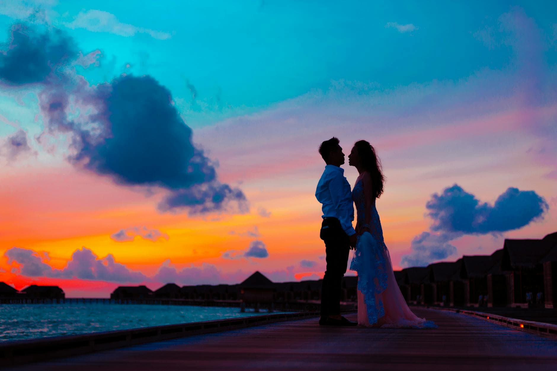 Silhouette of a couple embracing against a vibrant tropical sunset on a beach pier. - future goals couple