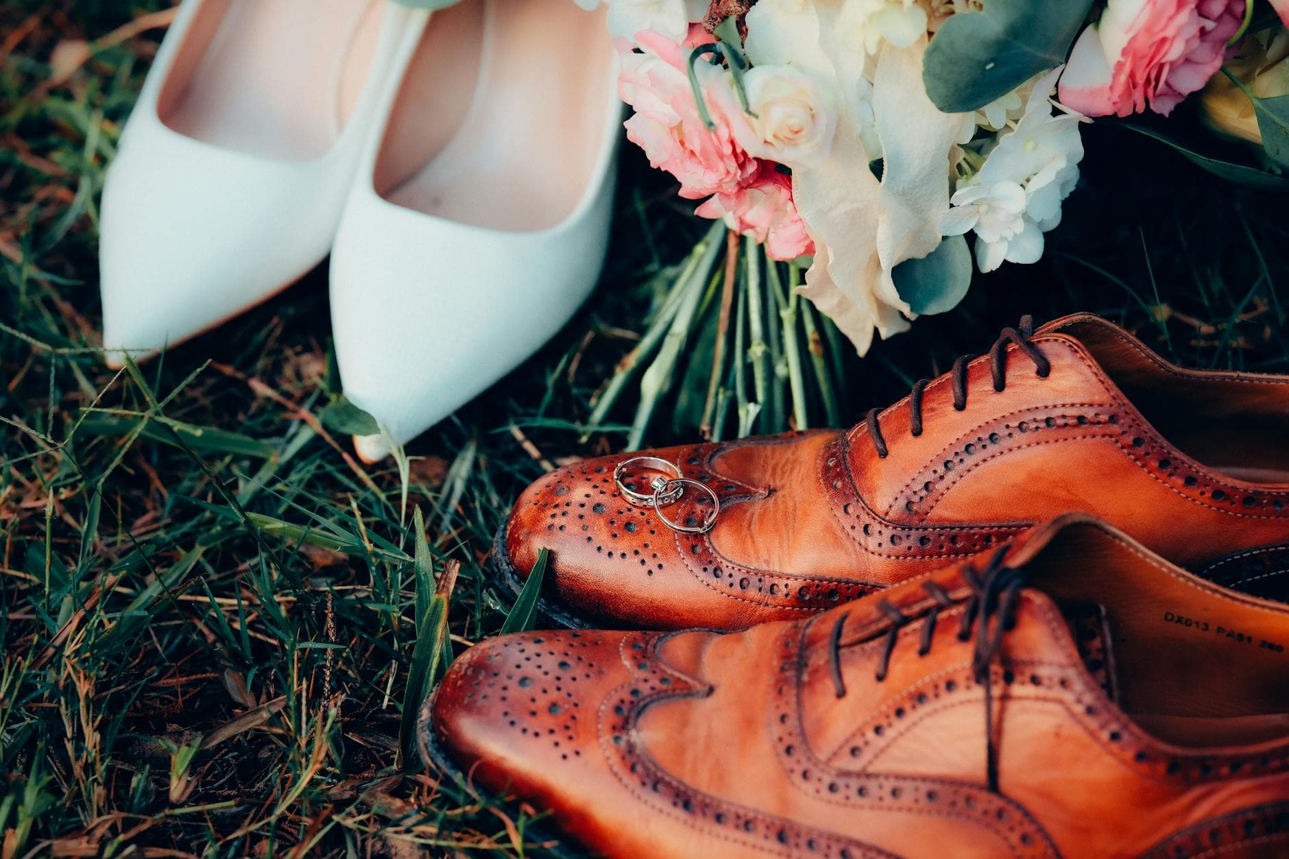 Close-up of wedding shoes and rings placed on grass with a floral bouquet, capturing a romantic outdoor setting. - marriage goals spring