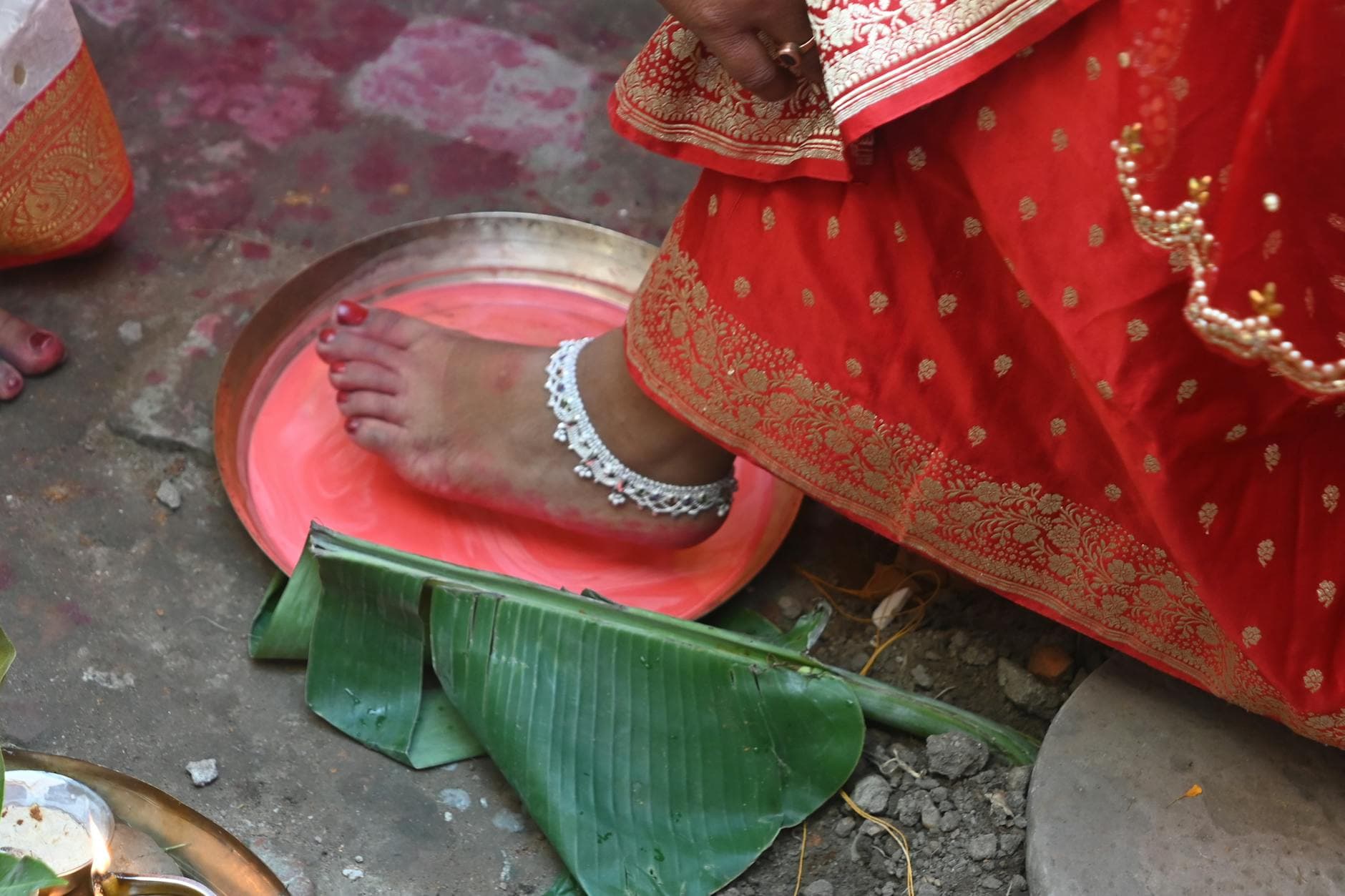 A close-up of a bride performing a traditional Indian wedding ritual involving colored water and banana leaves. - marriage traditions
