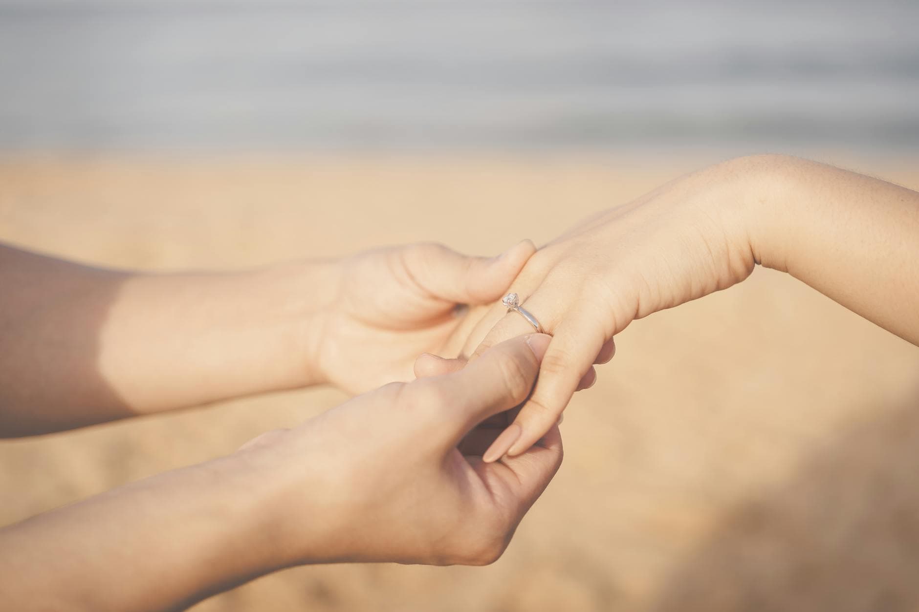Close-up of a beach proposal with a diamond engagement ring being placed on a finger. - marriage tune up
