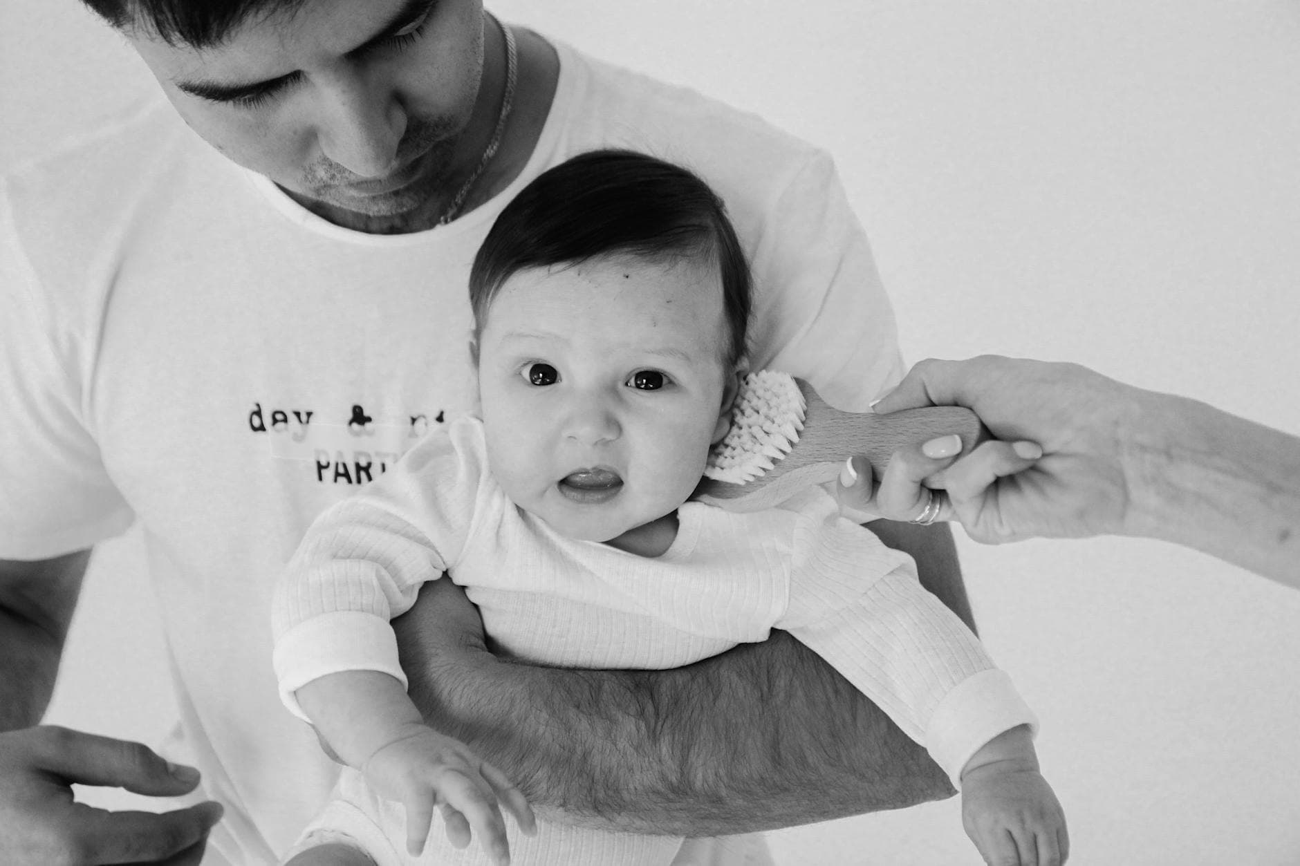 Black and white photo of a father holding a baby with another hand gently brushing the baby's hair. - new parent self care